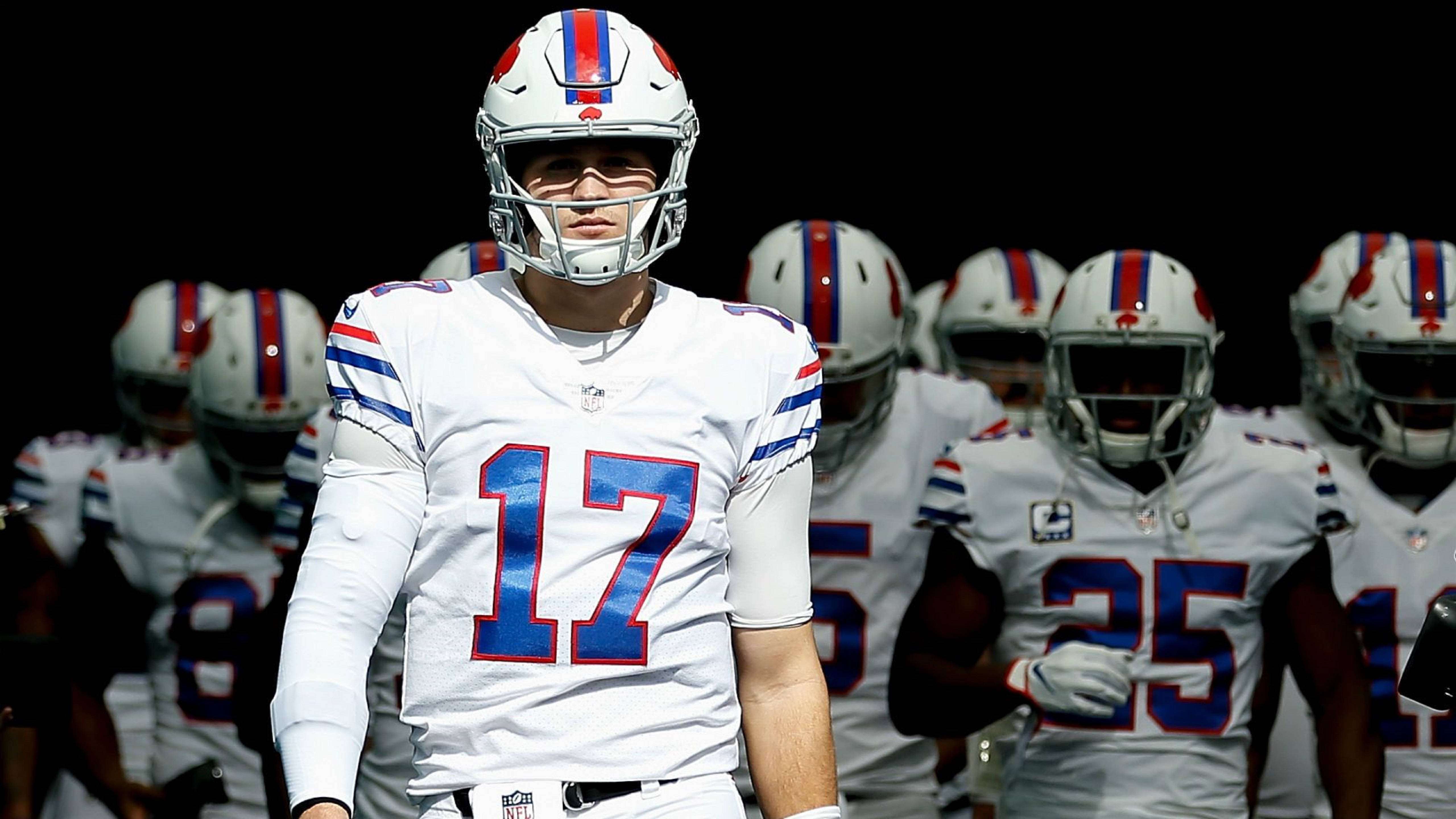 Josh Allen Buffalo Bills 球隊合照 壁紙 — 一名水牛城比爾隊的足球員（17號）站在身穿白色球衣的隊友前面，背景為黑色。