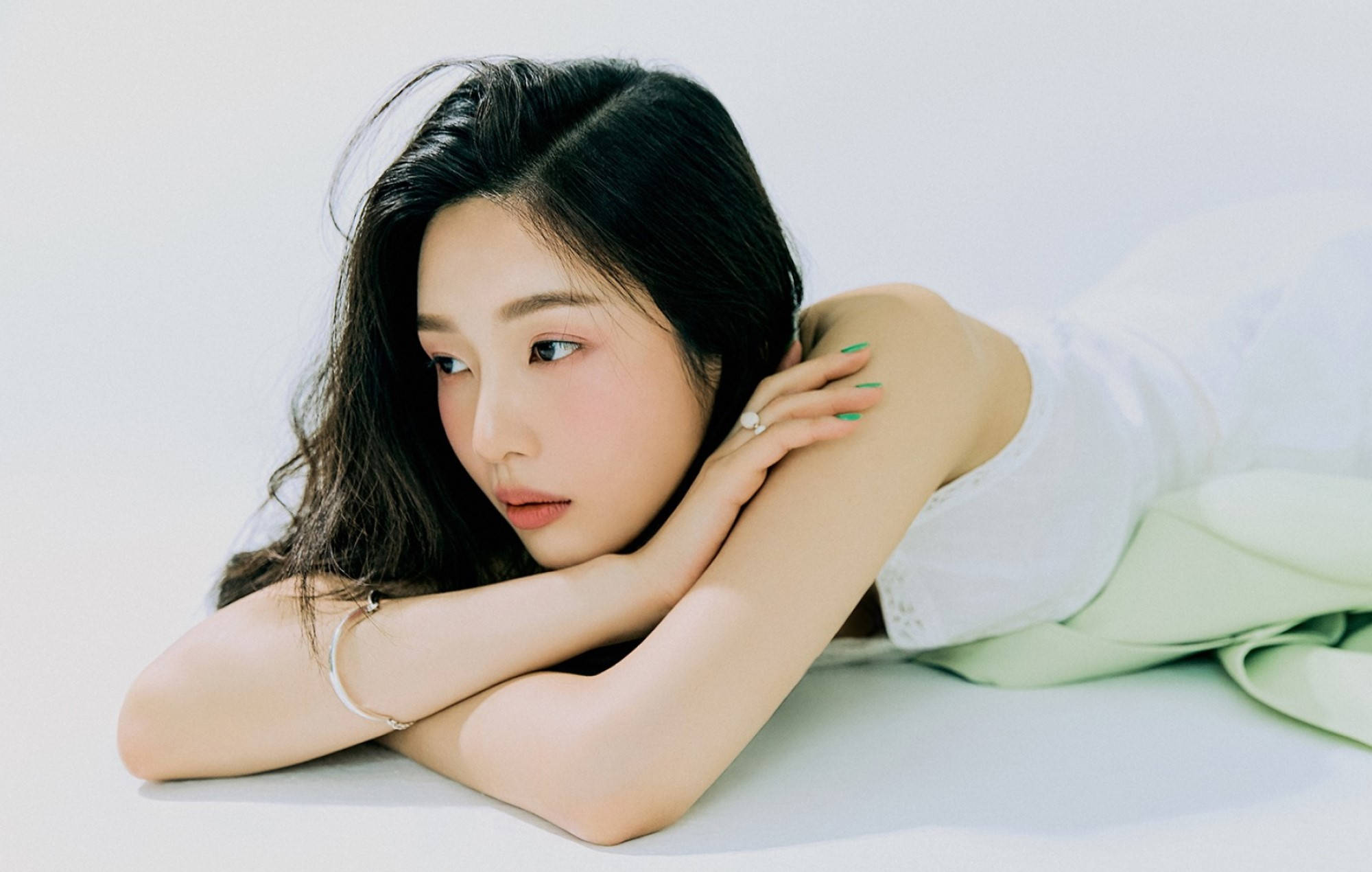 Joy 的 Sheesh 美學拍攝 壁紙 — 一位深色頭髮的年輕女子，在純白色背景上將下巴擱在手臂上，身穿白色上衣和淺綠色布料。