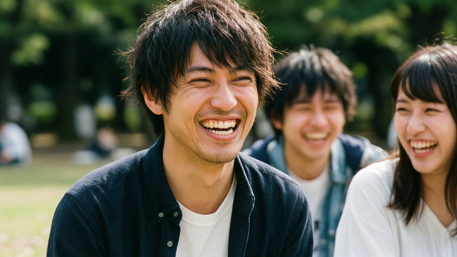 三個年輕朋友在陽光明媚的公園裡快樂地大笑，身後有綠樹