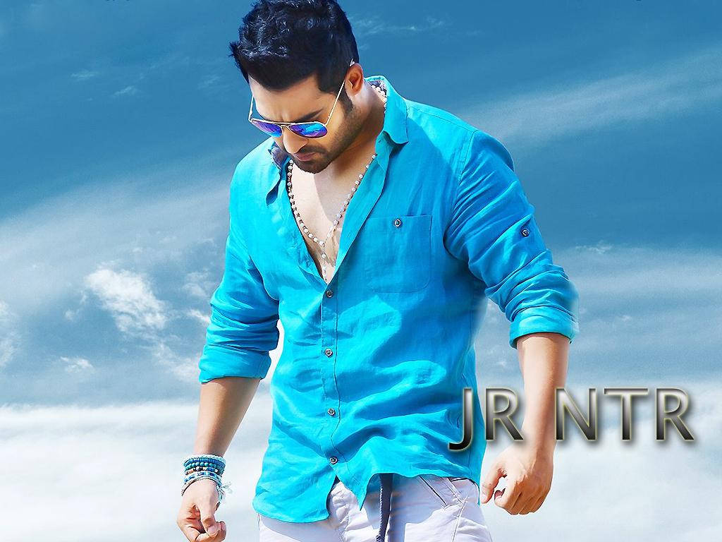 Jr Ntr 多雲天空 壁紙 — 一名身穿亮藍色襯衫和太陽眼鏡的男子，在帶有散雲的鮮豔藍天下自信地行走。