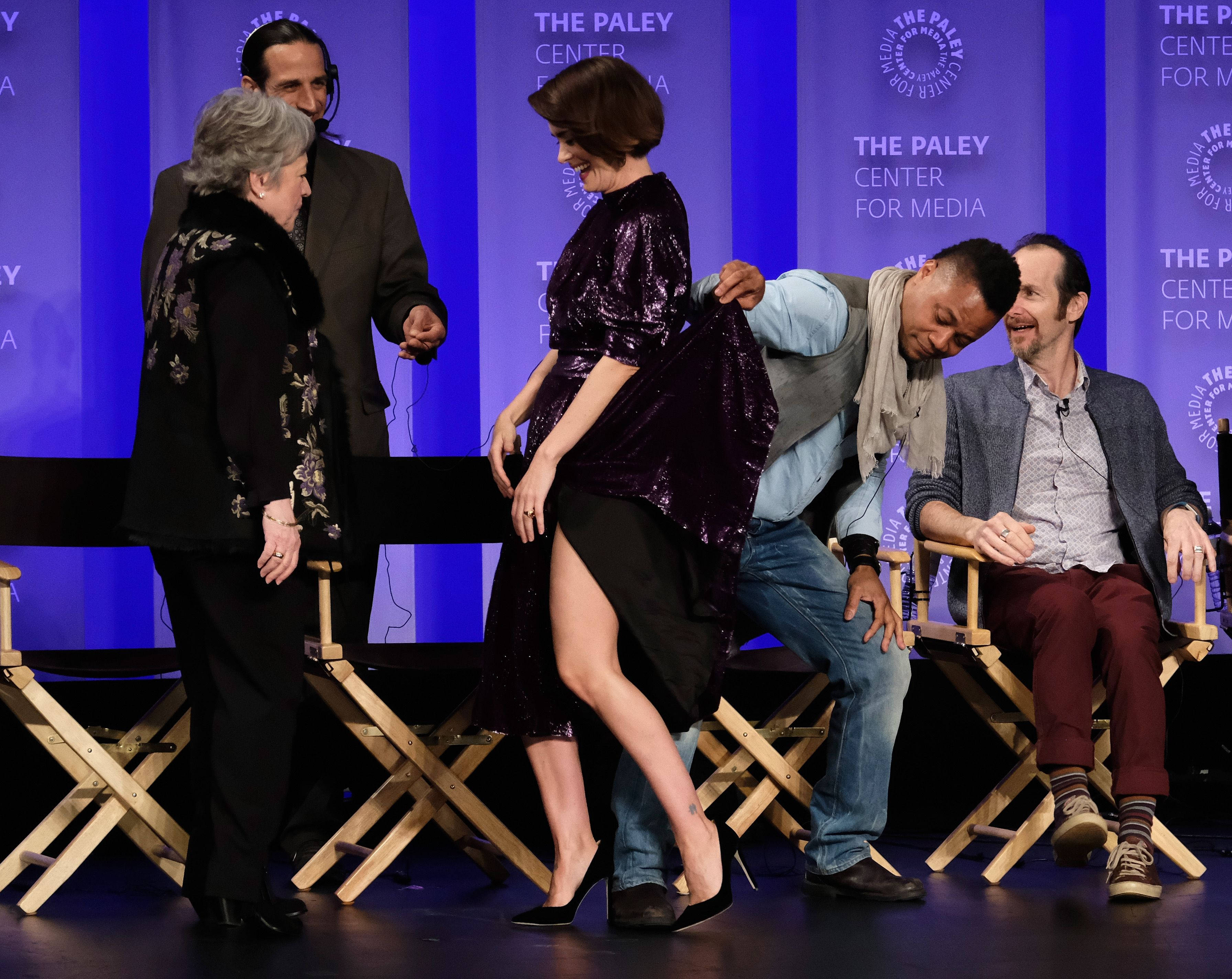 古巴·古丁 Jr. 在 PaleyFest 專場活動中 壁紙 — 一位穿著閃亮紫色連衣裙的女性大笑，因為一個男人在舞台上有坐著的客人和藍色背景的情況下頑皮地掀起她的裙子。