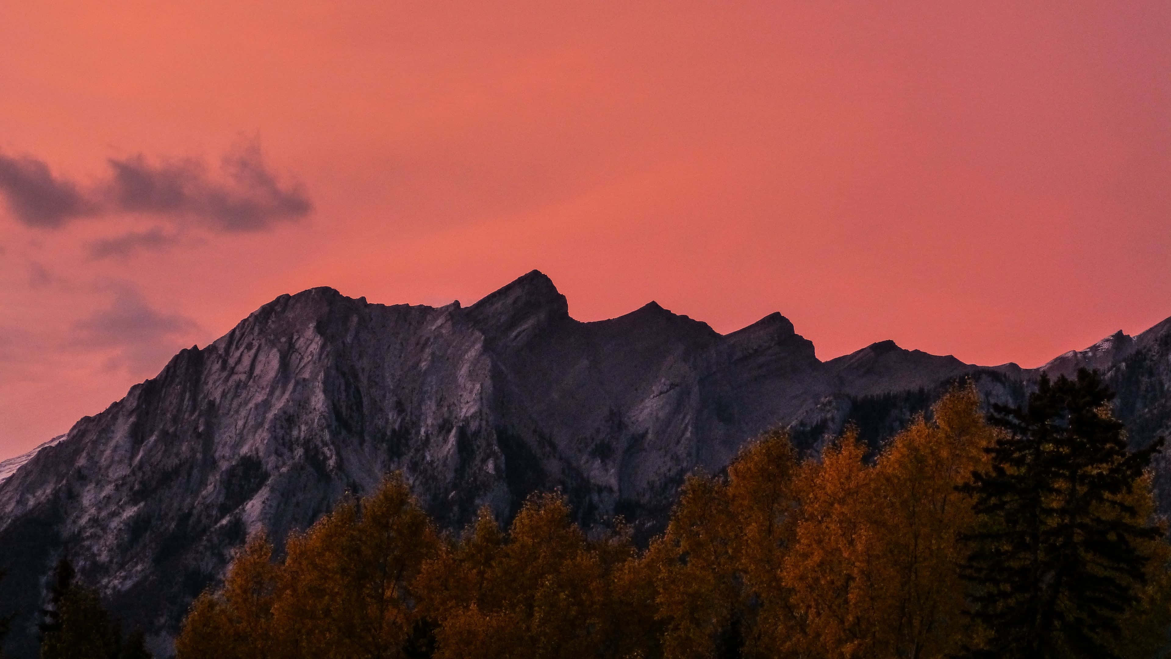 Colorful Sunset 桌布 壁紙 — 鋸齒狀山脈在火熱的粉紅色日落天空下形成剪影，前景是金色的秋樹。