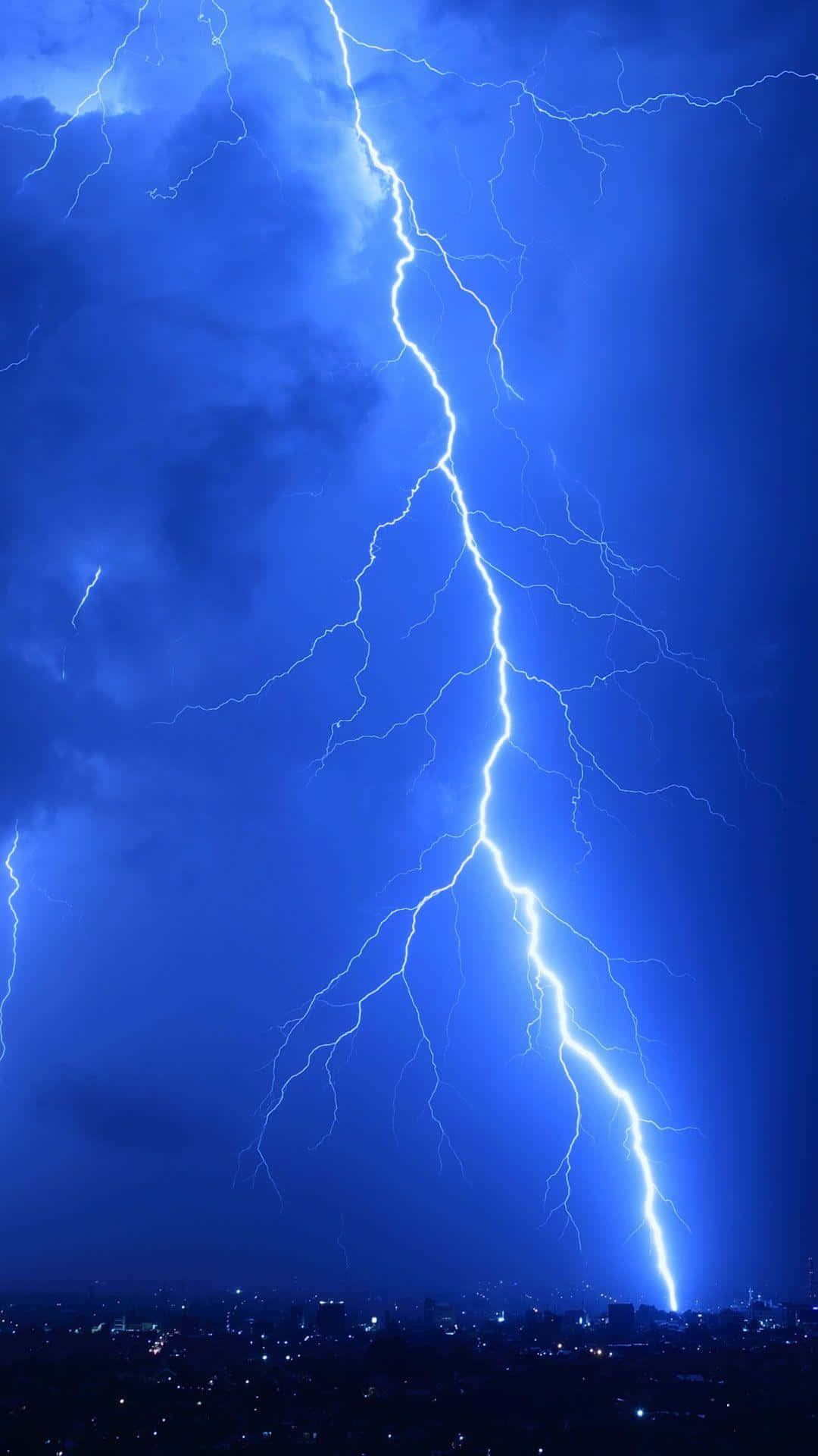 Lightning iPhone 桌布 壁紙 — 一道巨大的閃電在夜間城市景觀上方的深藍色暴風雨中分叉。