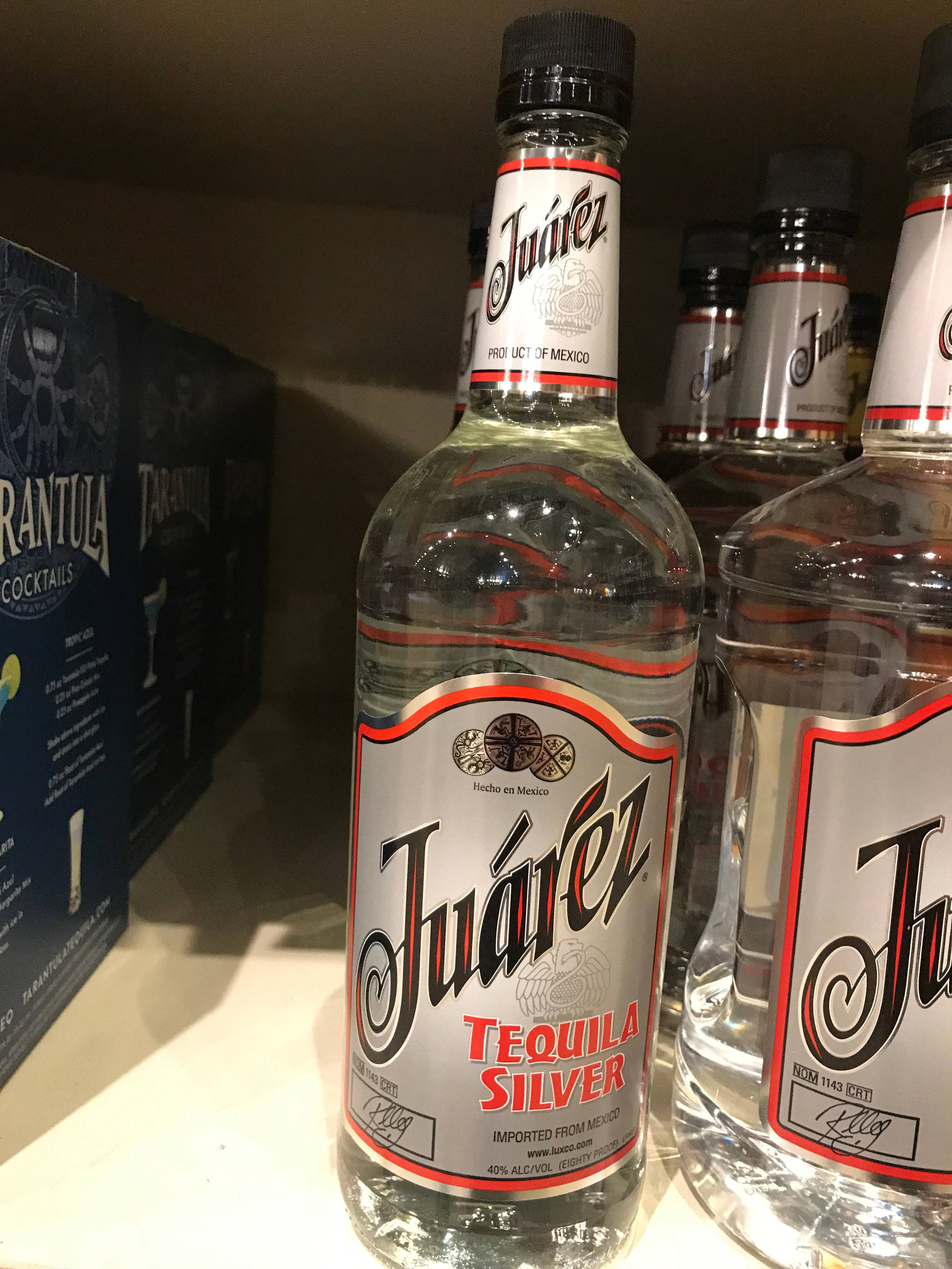 Juarez龍舌蘭酒銀色酒瓶架上陳列 壁紙 — 透明玻璃瓶的Juárez Tequila Silver整齊排列在架子上，背景有一個藍色雞尾酒盒。