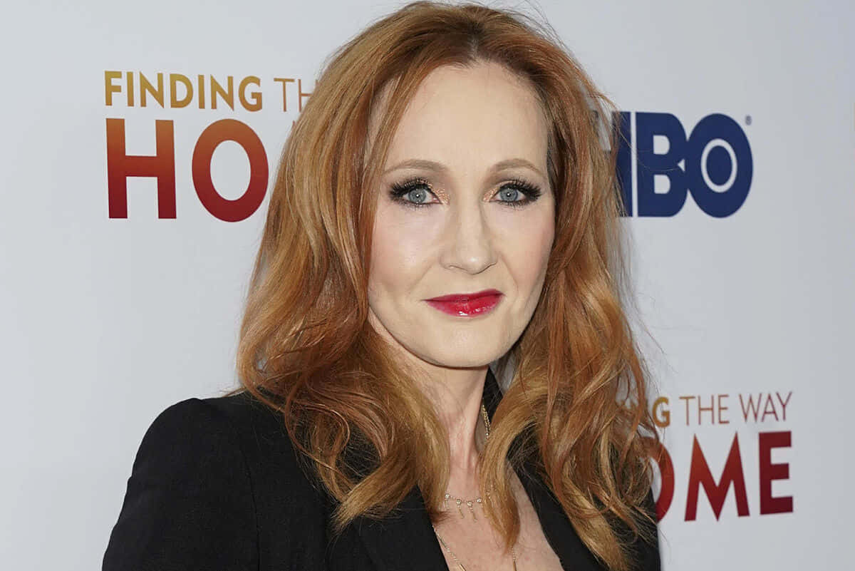 J K Rowling 桌布 壁紙 — Judy Kuhn 對著鏡頭微笑，紅髮和鮮紅的嘴唇，背景是HBO活動背景。