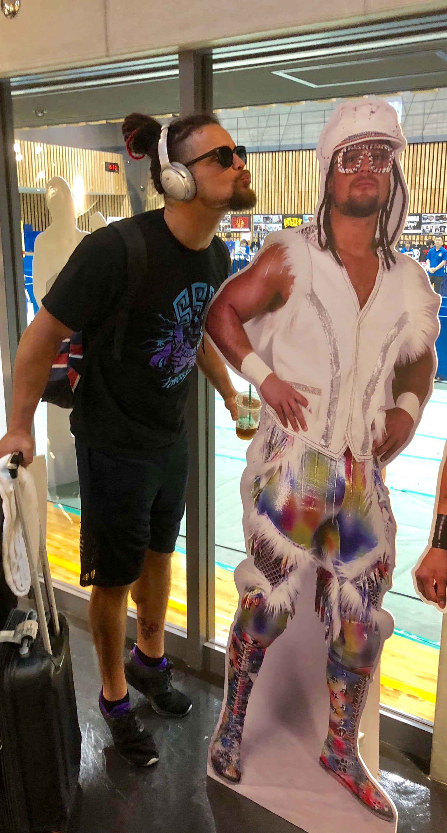 Juice Robinson 試吻立牌 壁紙 — 一名戴著耳機的男子站在現代室內空間中一個色彩繽紛的摔角手剪紙旁。