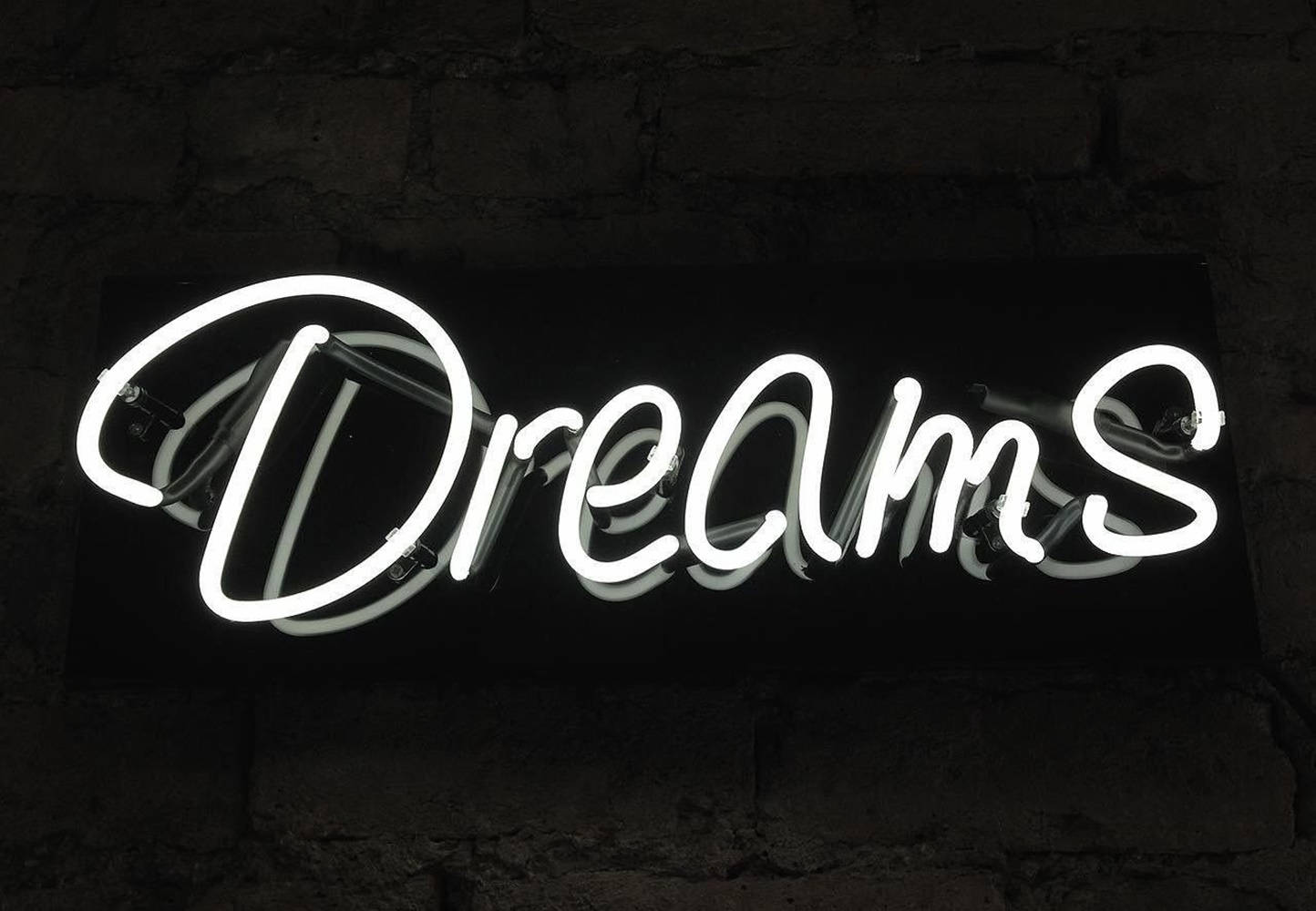 一個發光的白色霓虹燈牌，上面寫着 'Dreams'，安裝在深色磚牆上。