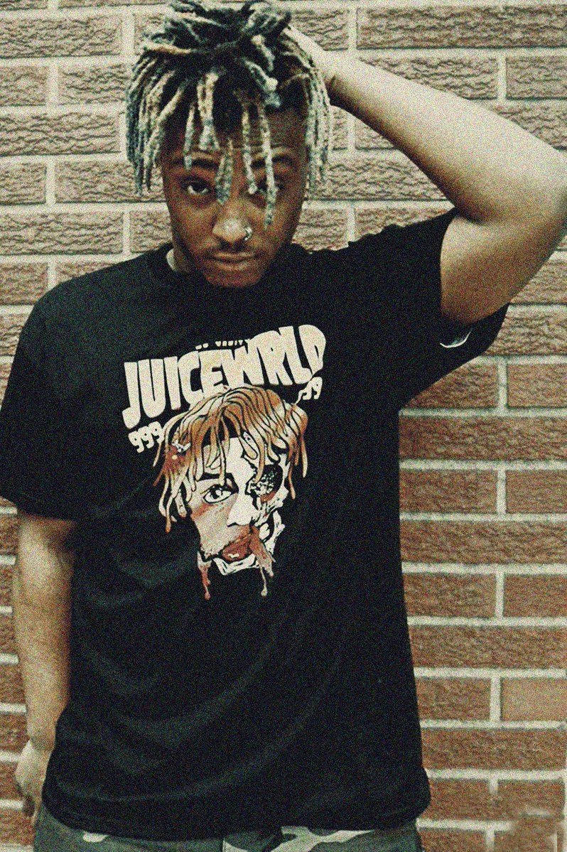 留著辮子的年輕男子身穿Juice WRLD T恤，站在磚牆前。