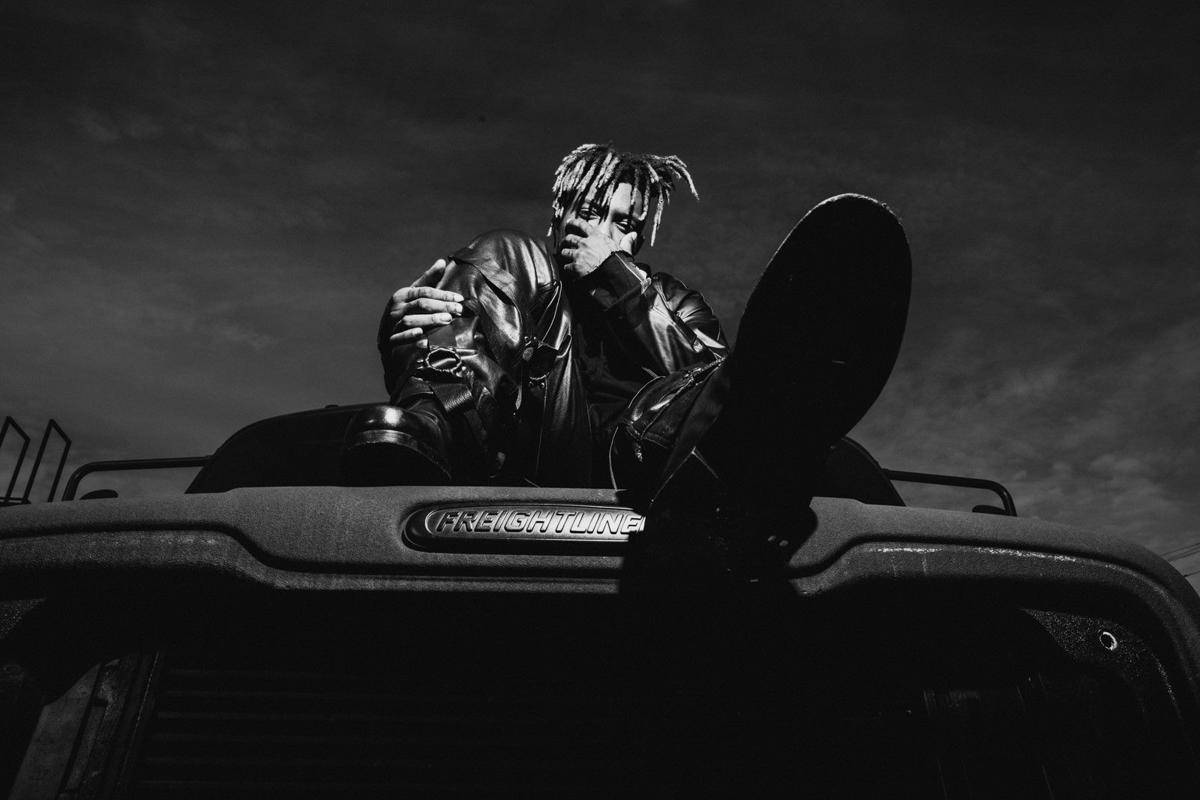 Juice Wrld 桌面汽車 壁紙 — 一名留著辮子的人坐在 Freightliner 卡車引擎蓋上，在戲劇性的單色燈光下拿著滑板。