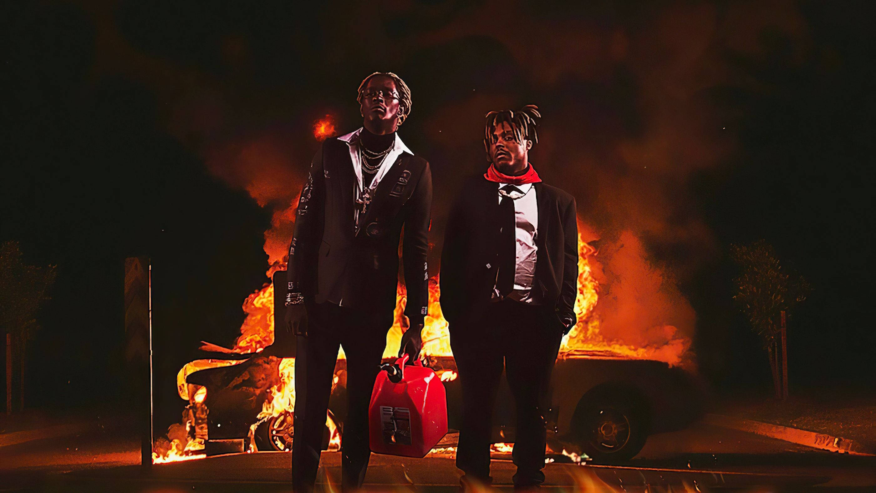 Juice Wrld 桌面火焰背景 壁紙 — 兩名身穿西裝的男子在夜間自信地站在一輛燃燒的汽車前，火焰將橙色光芒投射在他們的臉上。