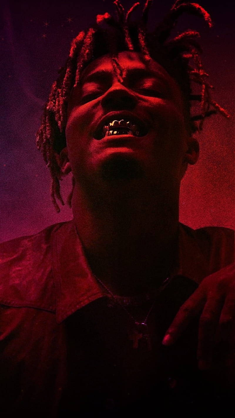 酷炫 Juice WRLD 展露金牙 壁紙 — 一個留著辮子頭、戴著金牙套的人，在強烈紅光下，以繁星點點的紫色背景微笑。