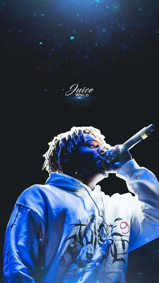 Juice Wrld 熱力四射的現場演出 壁紙 — Juice WRLD 在戲劇性的藍色舞台燈光下，熱情地對著麥克風表演，黑暗背景中有閃爍的粒子漂浮。