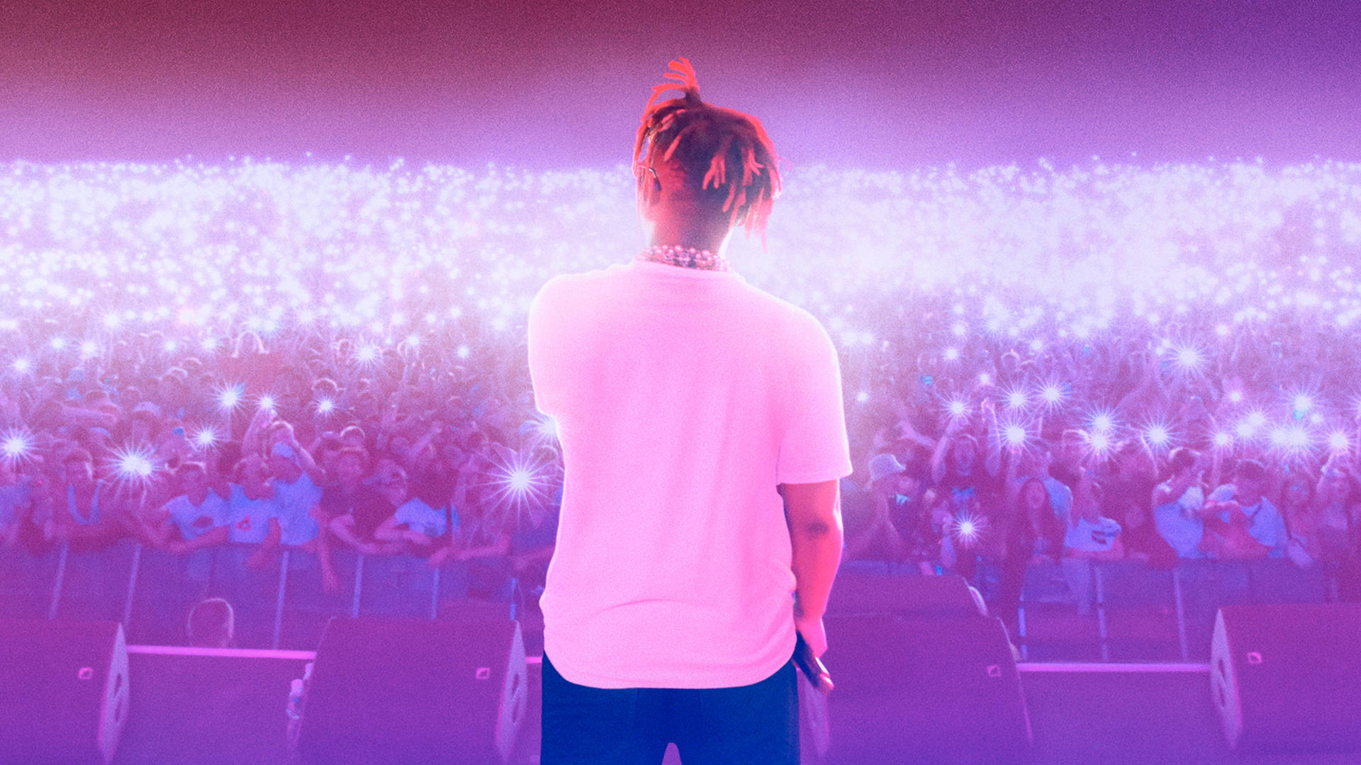 Juice Wrld 的不朽藝術——音樂界的傳奇 壁紙 — 一位表演者站在舞台上，背光照射著紫色燈光，面對著熱情觀眾手中閃爍的手機電筒燈海。