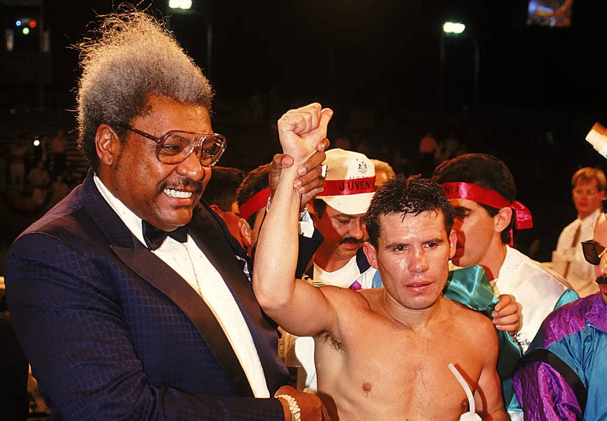 Julio César Chávez 勝利時 壁紙 — 一位勝利的拳擊手在競技場燈光下舉起拳頭，而一位微笑的官員宣佈他為勝利者。