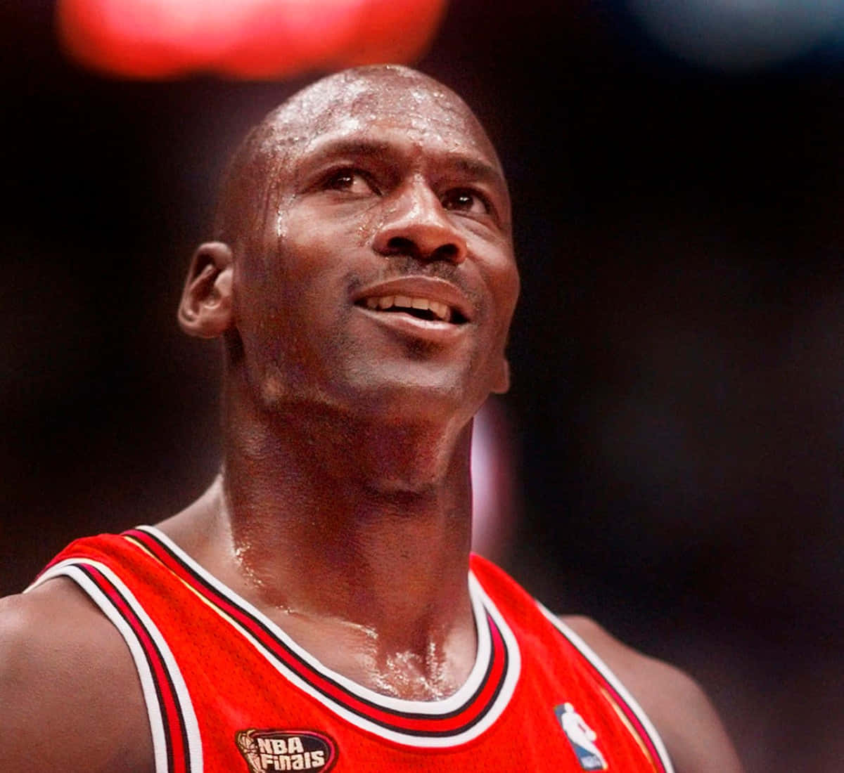 「邁克爾·喬丹——Jumpman」 壁紙 — 米高佐敦身穿紅色芝加哥公牛隊球衣，汗水淋漓，在明亮的場館燈光下於NBA總決賽比賽中向上仰望。