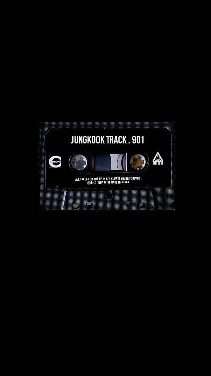 Jungkook磁帶暗黑龐克風 壁紙 — 一盒復古黑色卡式錄音帶，中央印有「JUNGKOOK TRACK . 901」字樣，置於帶有像素紋理的漆黑背景上。
