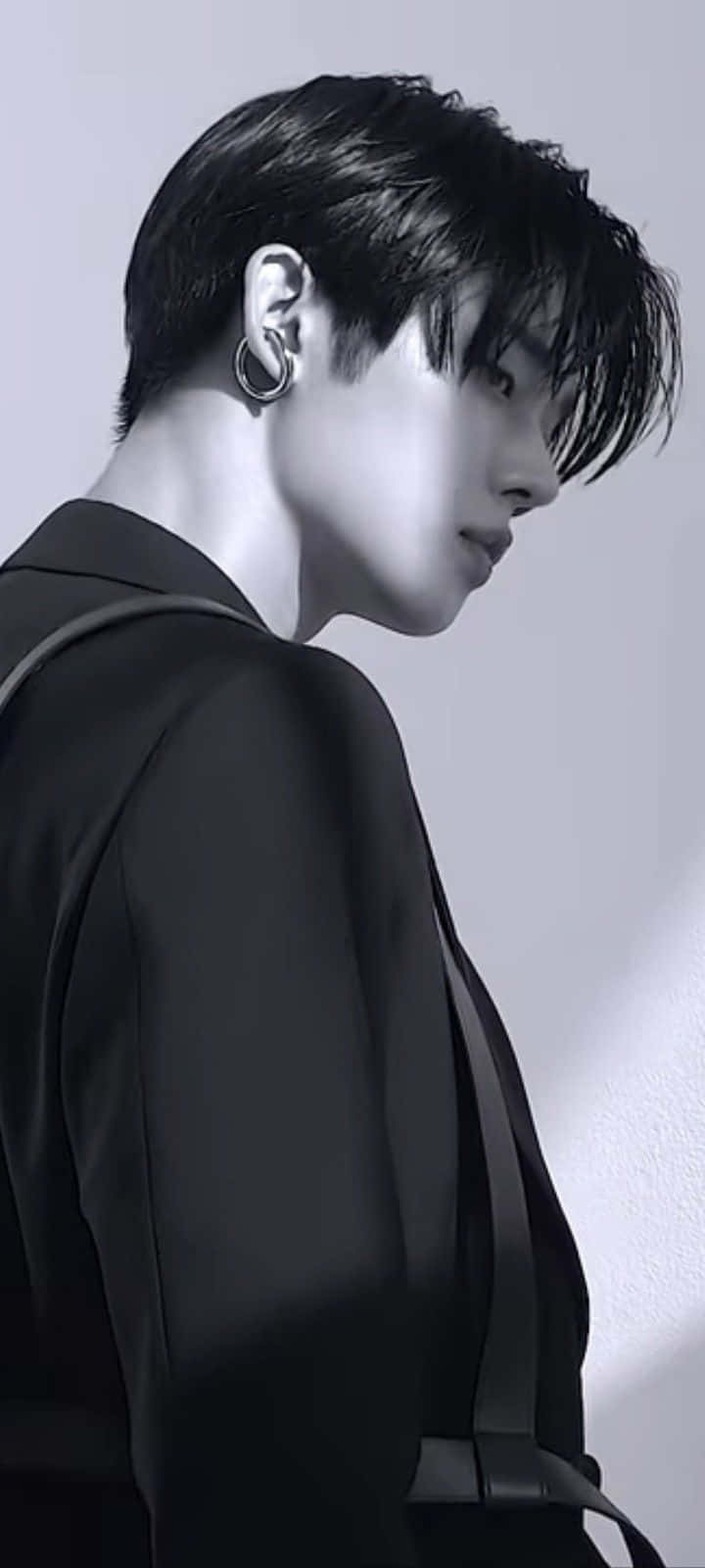 Jungkook時尚攝影 壁紙 — 一幅黑白側面肖像，年輕男子身穿黑色西裝外套，戴著圈形耳環，背景是素牆。