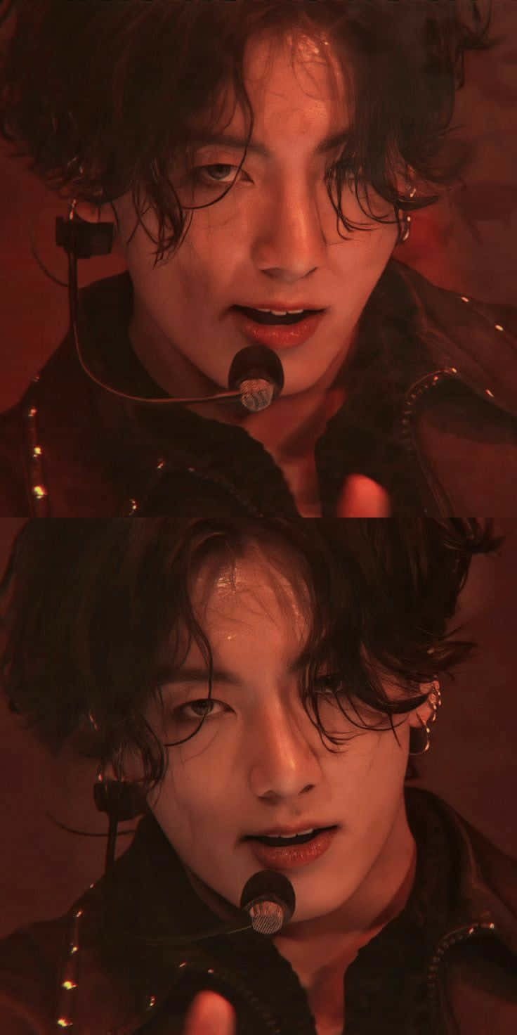 Jungkook：才華洋溢的BTS歌手 壁紙 — 一位表演者濕著深色頭髮在溫暖的紅色舞台燈光下對著麥克風唱歌的特寫。