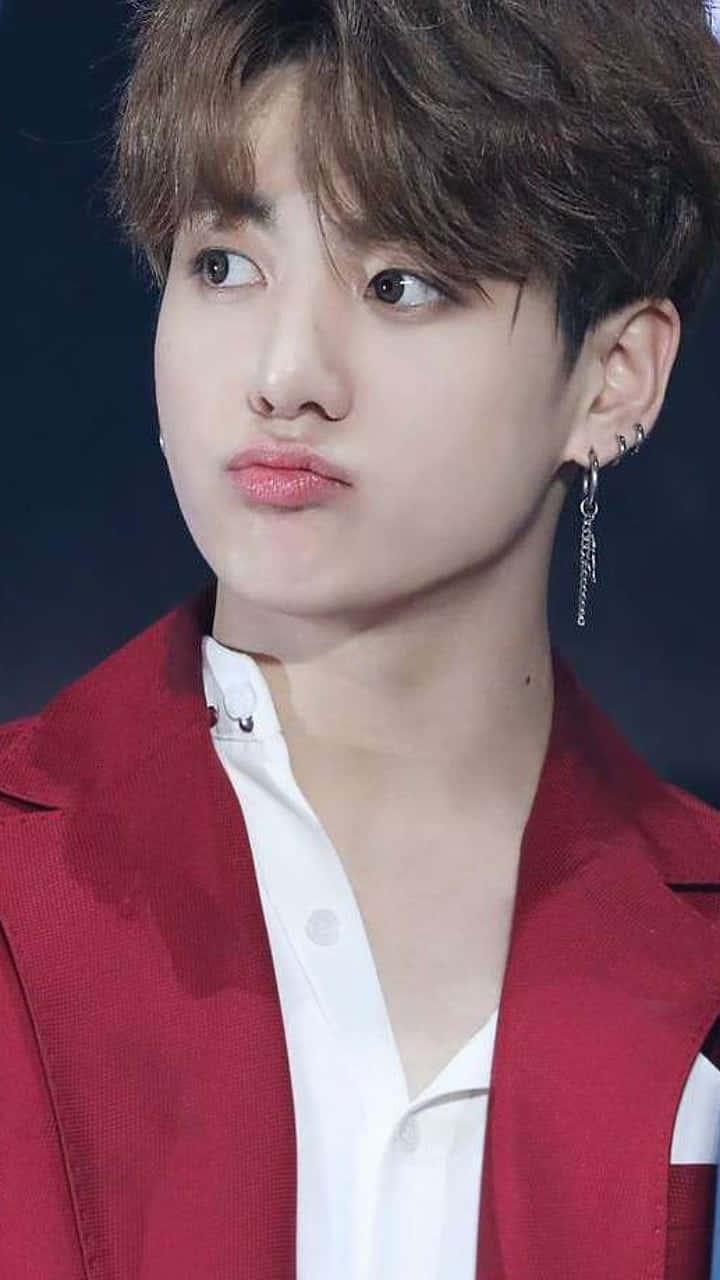 Jungkook以迷人氣場征服粉絲 壁紙 — 一個年輕男子嘅特寫肖像，佢有亂糟糟嘅棕色頭髮，著住紅色西裝外套同白色恤衫，背景係黑色。
