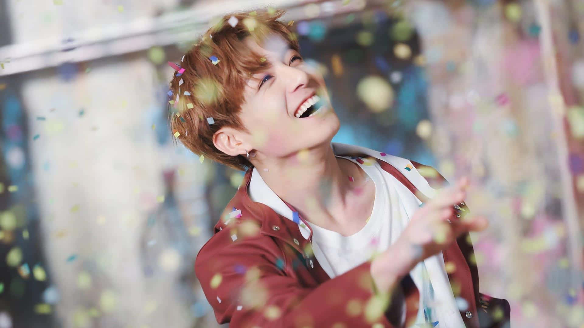 Jungkook出席《Burn The Stage: The Movie》拍照活動 壁紙 — 一個快樂的年輕男子閉著眼睛大笑，色彩繽紛的紙屑在他周圍如雨般落下，在明亮的室內環境中。