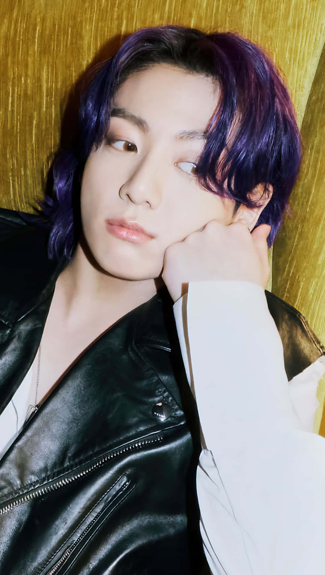 Jungkook專注凝視前方，目光堅定 壁紙 — 一位年輕男子擁有鮮豔紫色頭髮，穿著黑色皮夾克，在紋理金色背景上將頭靠在手上。