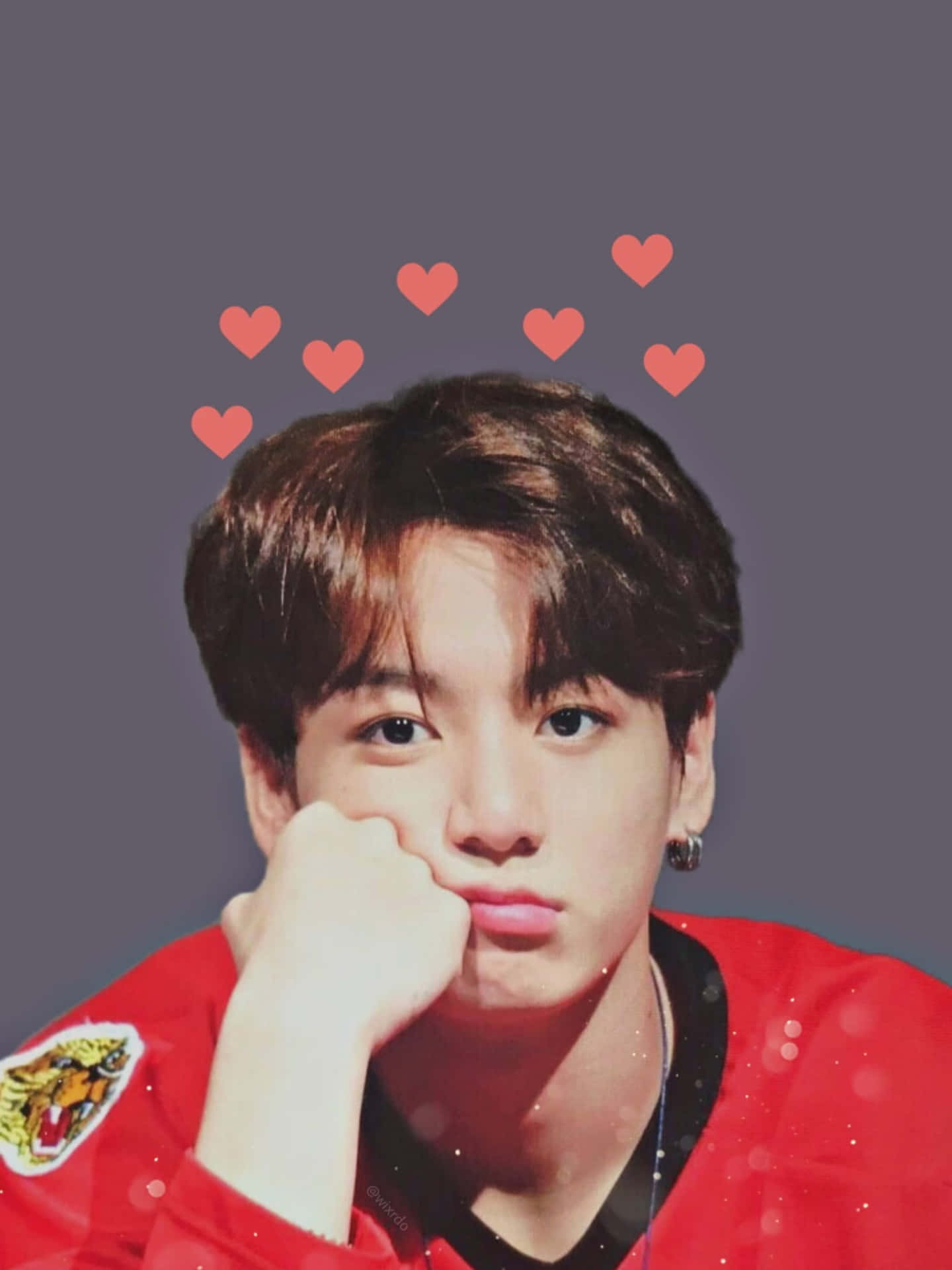 Jungkook於攝影棚展現自信與魅力 壁紙 — 一名身穿紅色外套的年輕男子，手托下巴，頭頂上方漂浮著心形圖案，背景為灰色。