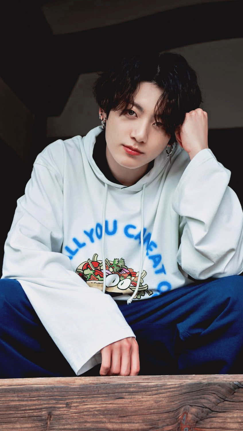 Jungkook於舞台展現迷人笑容 壁紙 — 一位黑髮年輕男子穿著帶有沙律圖案的連帽衫，隨意地坐著，直視鏡頭。