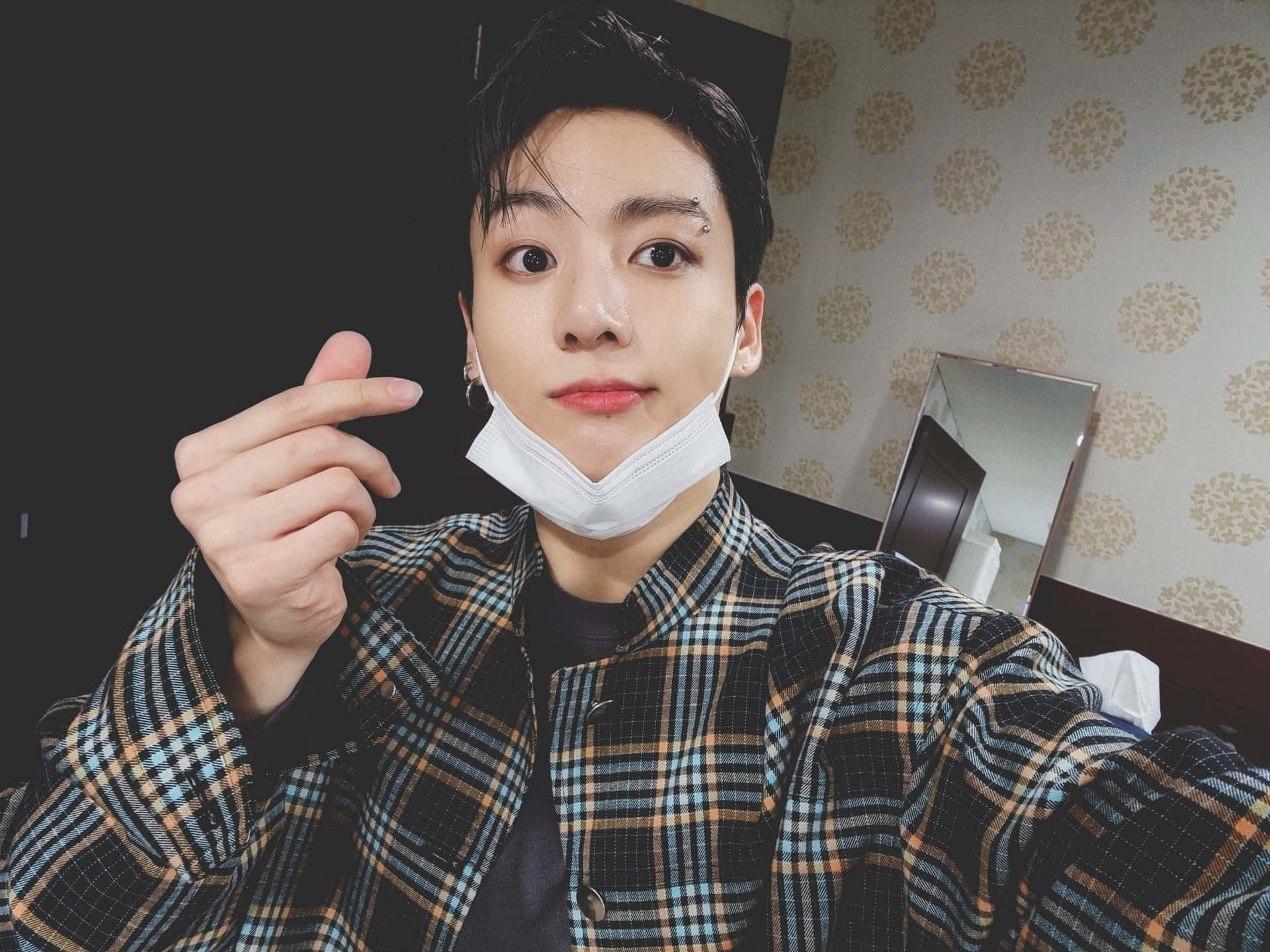 Jungkook於電光舞台展現震撼演出 壁紙 — 一位年輕男子拉下口罩，微笑並指向相機，房間內有圖案牆紙。