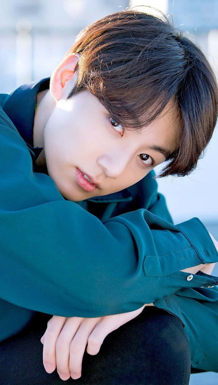 Jungkook於高質感壁紙中展現迷人風采 壁紙 — 一位深色頭髮的年輕男子穿著青綠色襯衫，在明亮模糊的背景前向前傾身。