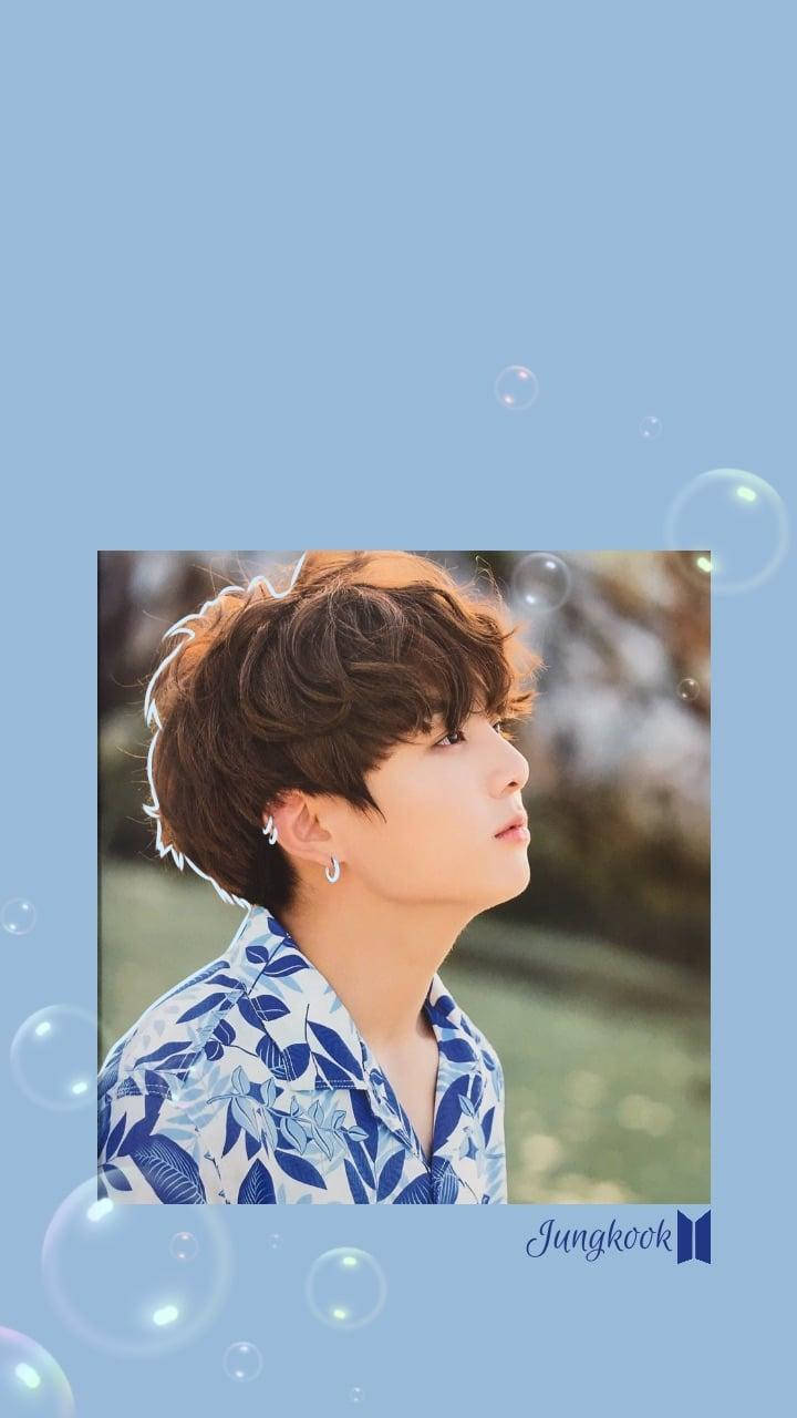 Jungkook時尚泡泡 壁紙 — 年輕男子留著棕色捲髮，身穿藍色花卉襯衫，在柔和藍色背景中仰望，周圍有漂浮的氣泡。