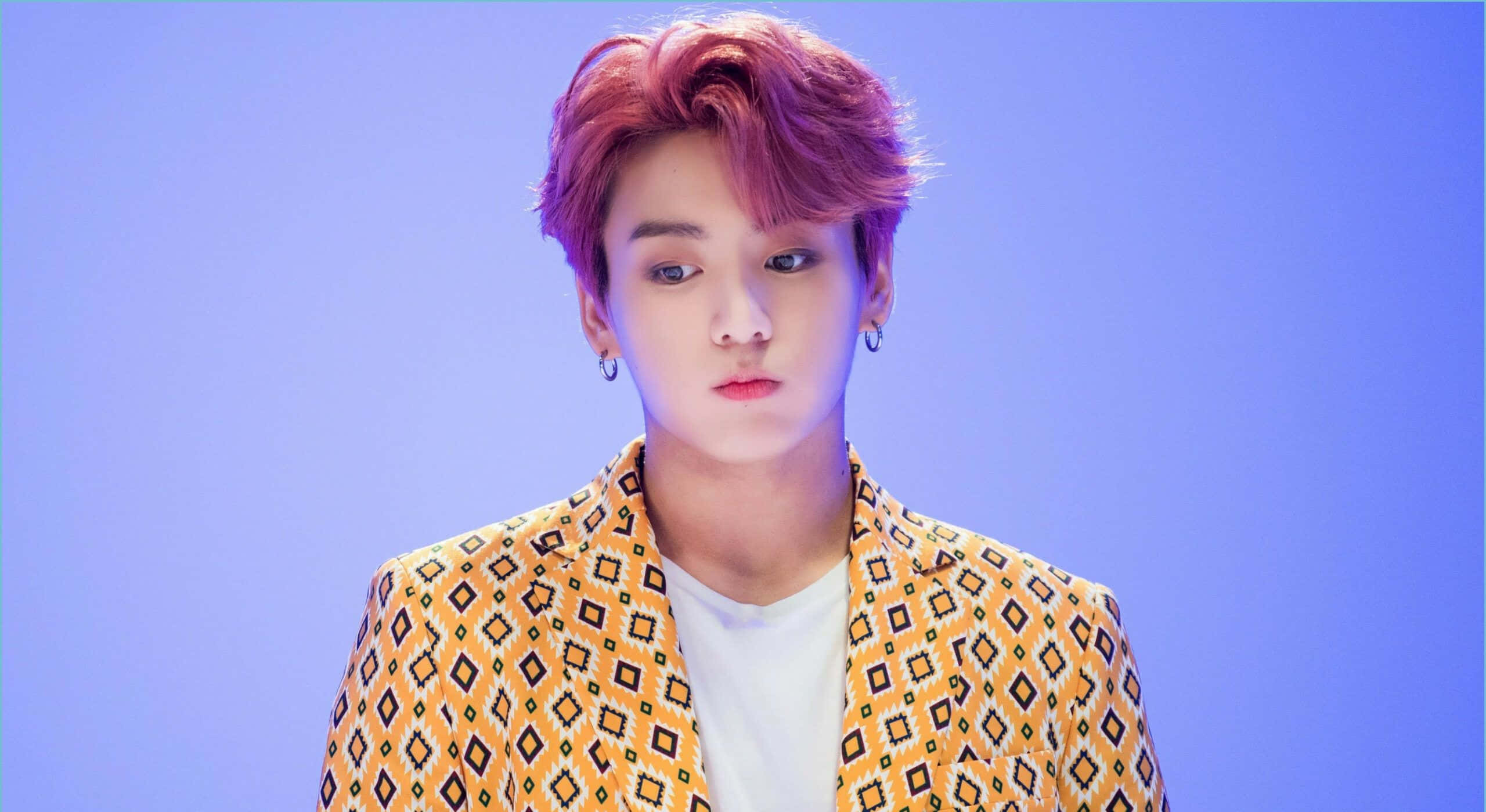 Jungkook深邃凝視，氣質迷人 壁紙 — 一位粉紅色頭髮的年輕男子穿著圖案黃色西裝外套，背景為純藍色。