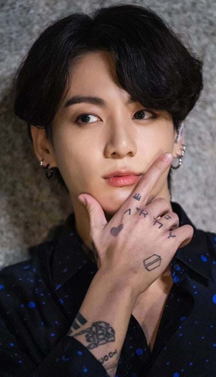 Jungkook舞台上的耀眼姿態 壁紙 — 一位深色頭髮、有紋身的年輕男子，輕輕將臉貼在紋理灰色牆上。