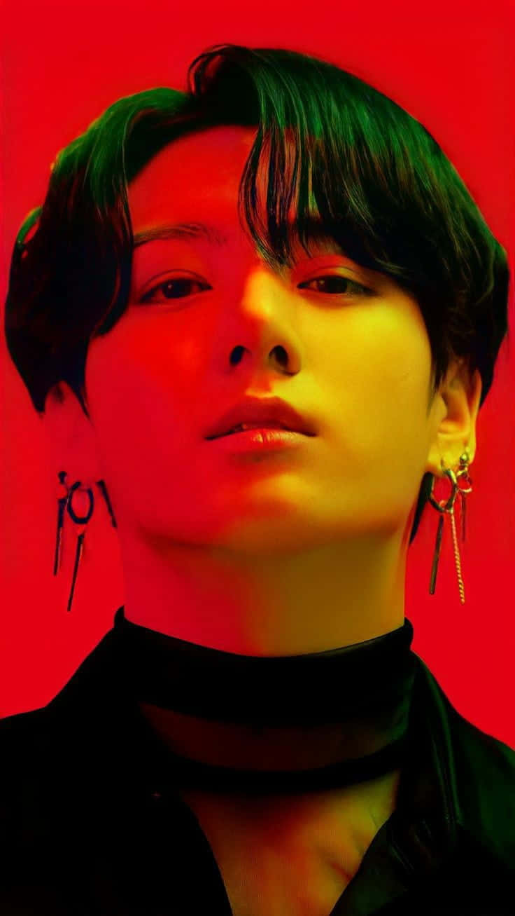 Jungkook遠眺微笑特寫 壁紙 — 一位深色頭髮、戴著耳環的人，在鮮紅色背景與戲劇性的綠色和黃色燈光下，強烈地凝視著。