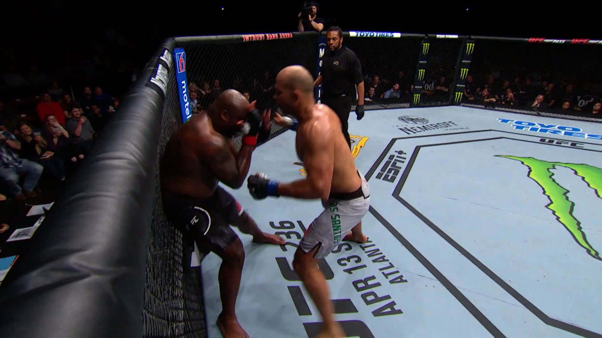 Junior Dos Santos 對戰 Derrick Lewis 壁紙 — 兩名拳手在明亮的場館燈光下於UFC八角籠中交鋒，裁判和觀眾專注觀看。