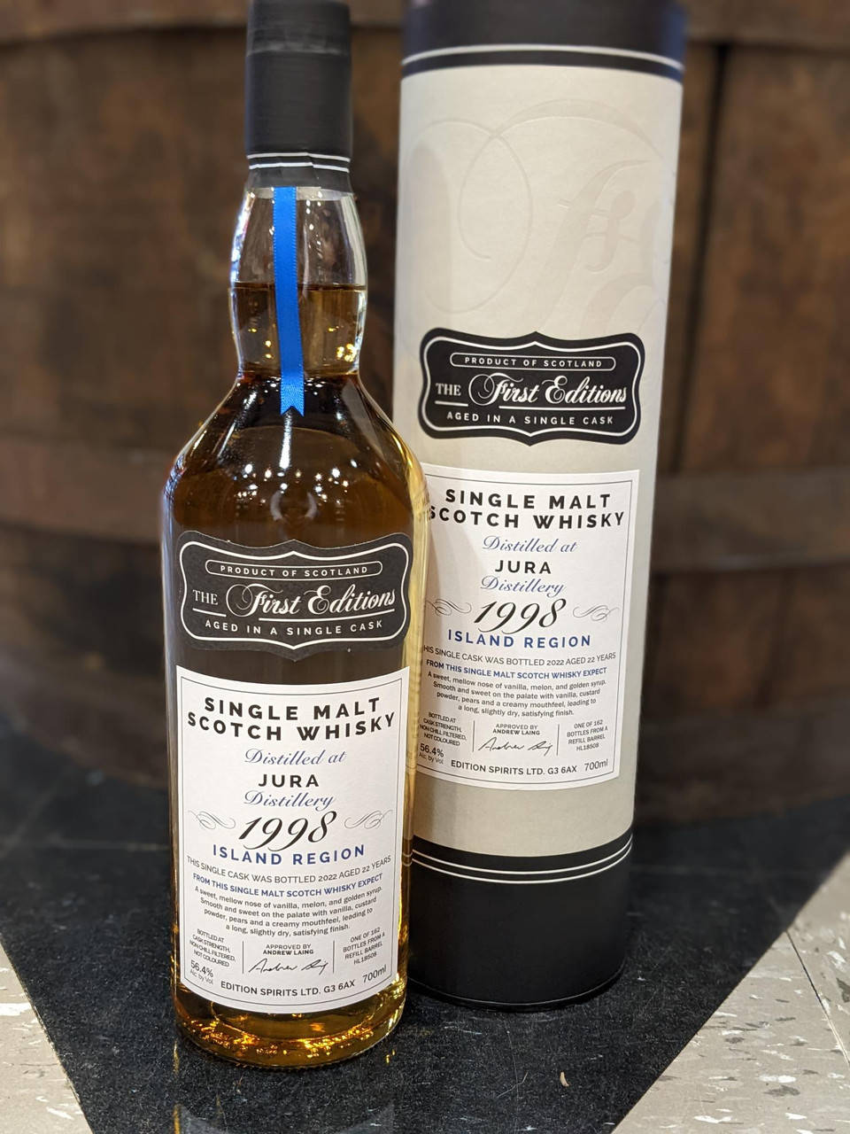 Jura Talisker 单一麦芽苏格兰威士忌 壁紙 — 一瓶1998年Jura單一麥芽蘇格蘭威士忌連同其管狀包裝，放置在深色大理石表面上，背景為木質。