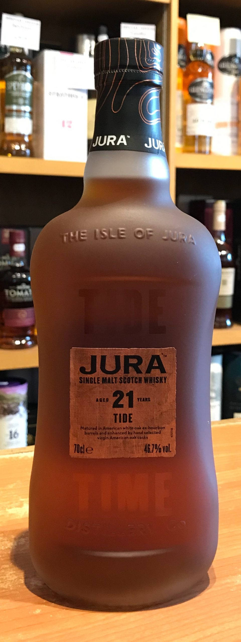 Jura 島 Old Tide 苏格兰威士忌 壁紙 — 一瓶結霜的 Jura 21 年單一麥芽蘇格蘭威士忌放在木質表面上，背景有陳列其他烈酒的層架。
