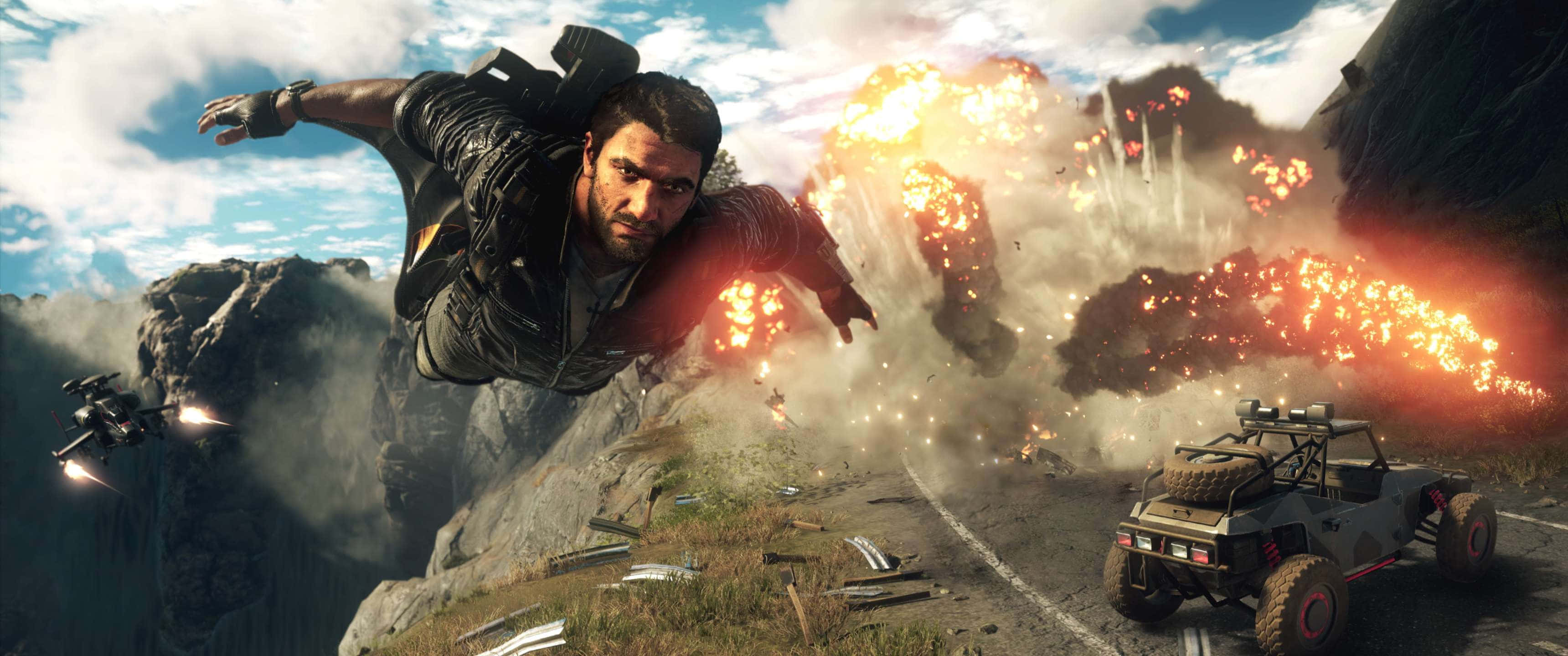 《Just Cause 4》主角里科·羅德里格斯 3440x1440p 壁紙 — 一個男人飛越山峽，身後爆炸四起，一輛堅固的車輛在下方蜿蜒的道路上疾馳。