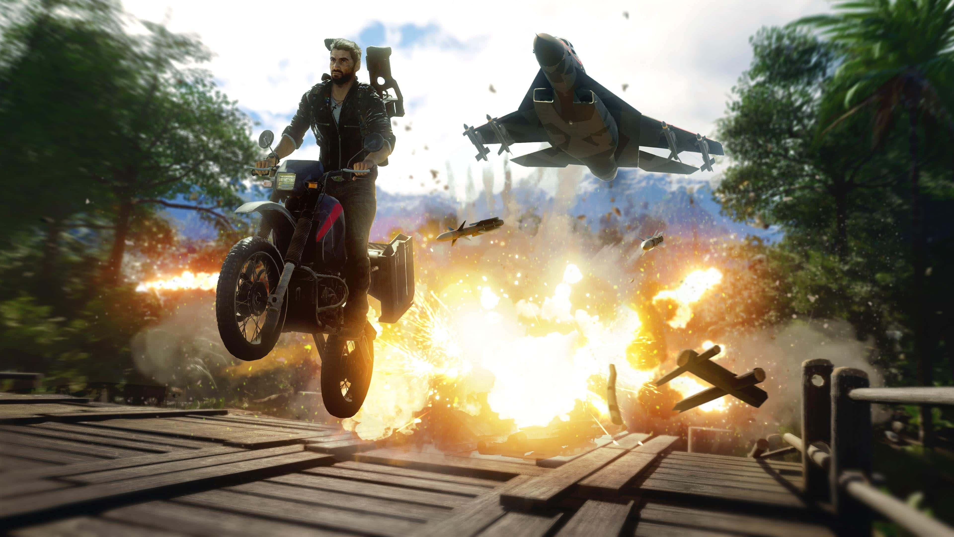 《Just Cause 4》最佳背景：里科騎摩托車穿過橋樑 壁紙 — 一個鬍鬚男騎著電單車駛過一條木橋，橋下發生爆炸，一架戰鬥機在叢林環境中飛過頭頂。