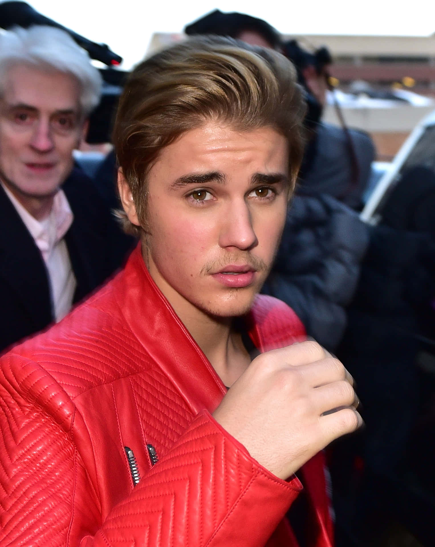 Justin Bieber 在戶外活動中穿著紅色皮革外套，身旁有狗仔隊。