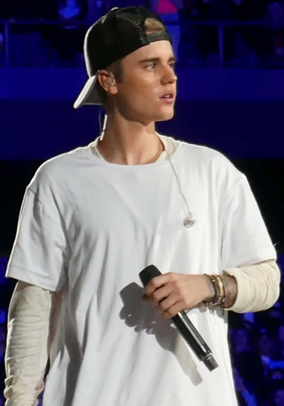 Justin Bieber 在藍色燈光的音樂會舞台上對著麥克風唱歌。