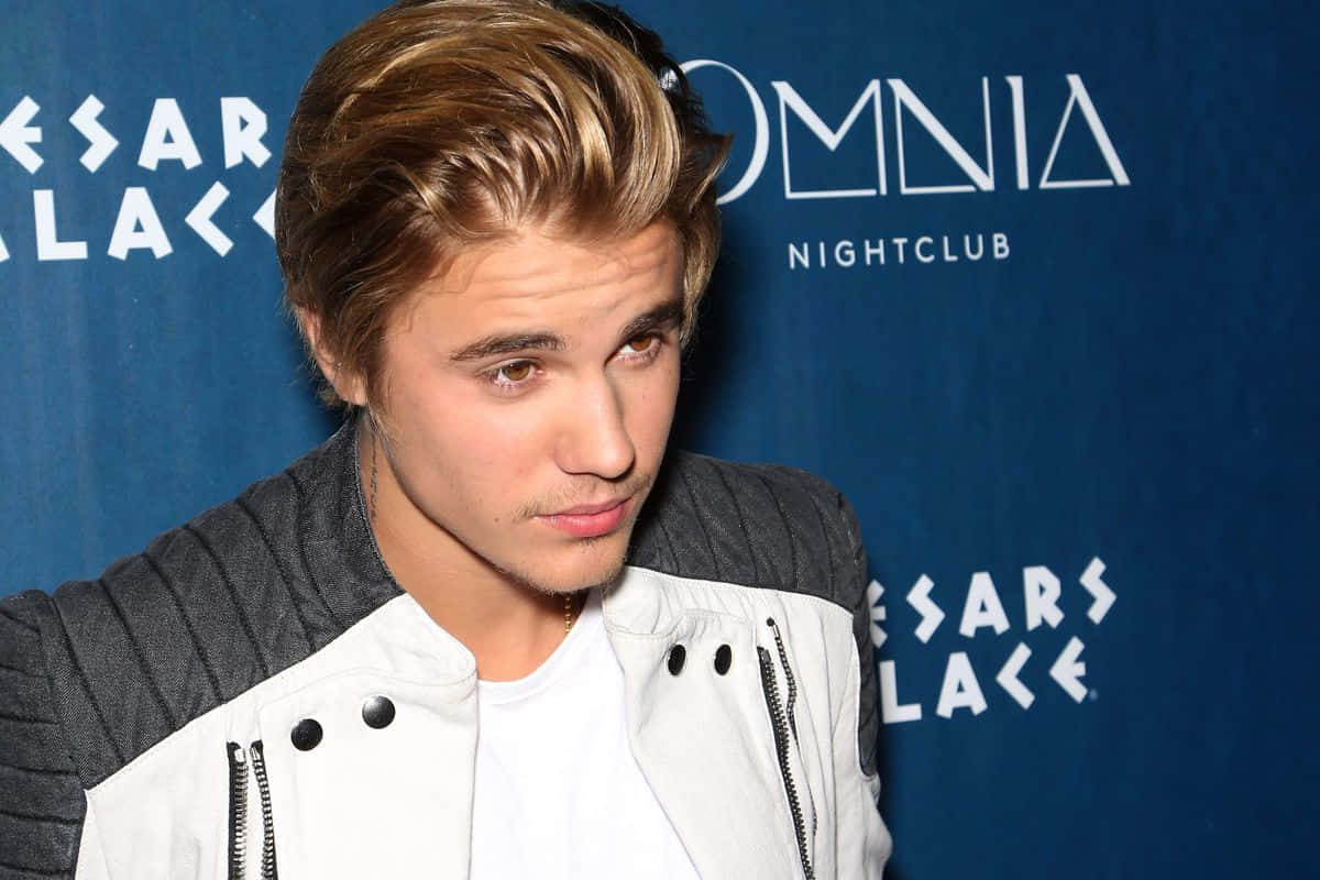 Justin Bieber, 2015 壁紙 — Justin Bieber 穿著白色和灰色外套，在藍色品牌背景前望向鏡頭外。