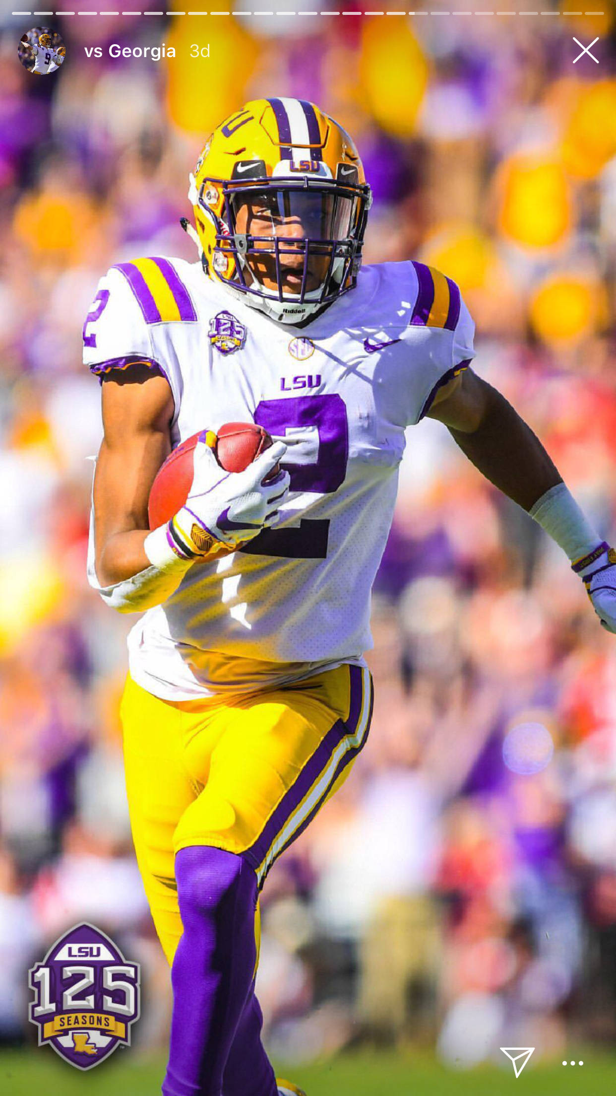 Justin Jefferson 賽場瞬間 壁紙 — 一名身穿白色和紫色球衣的LSU足球員在日間比賽中持球衝刺，背景是模糊的人群。