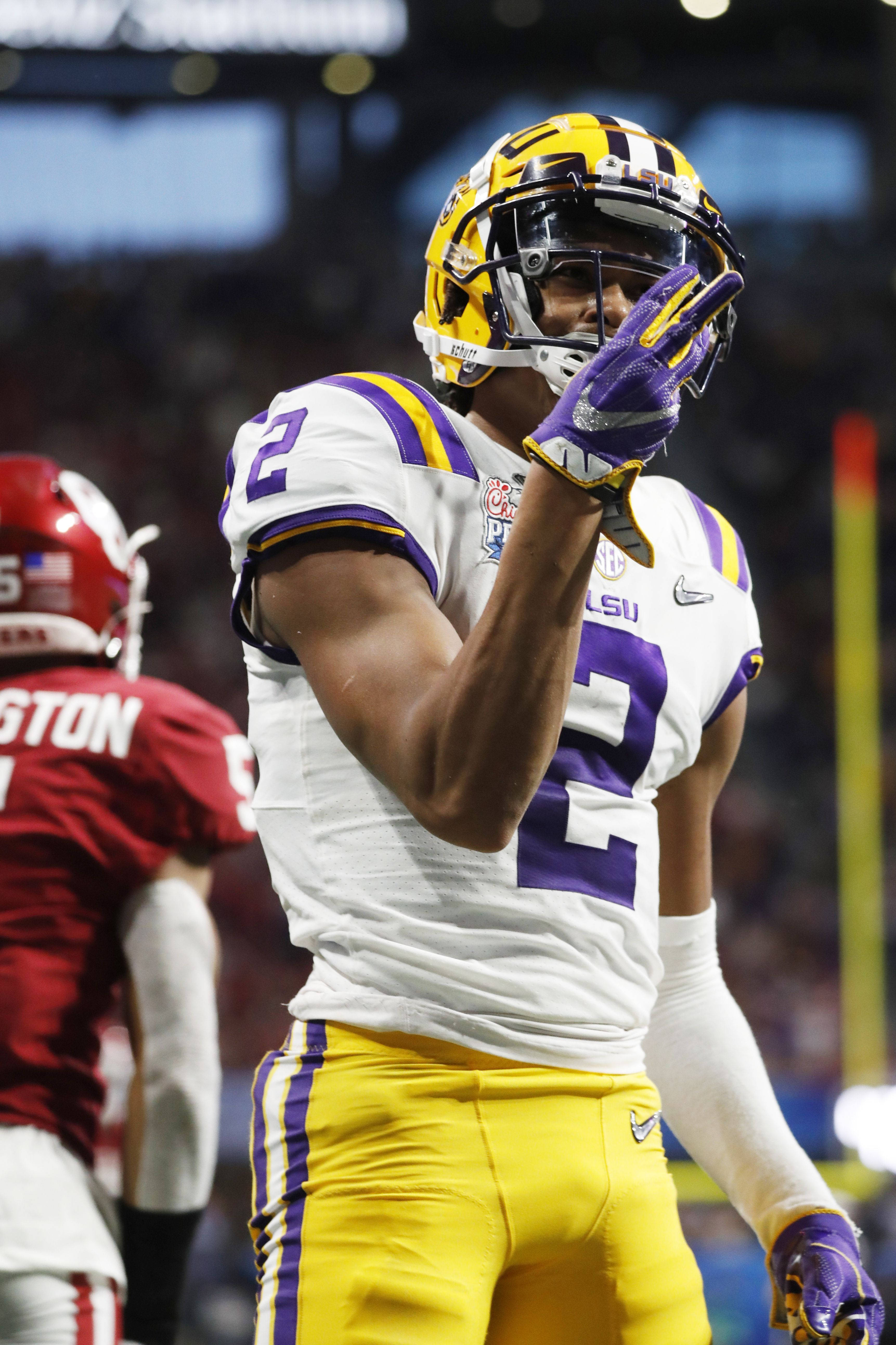 Justin Jefferson 美式足球員 壁紙 — 一名身穿白色、紫色和金色球衣的LSU足球員在夜間比賽中於球場燈光下舉手慶祝。