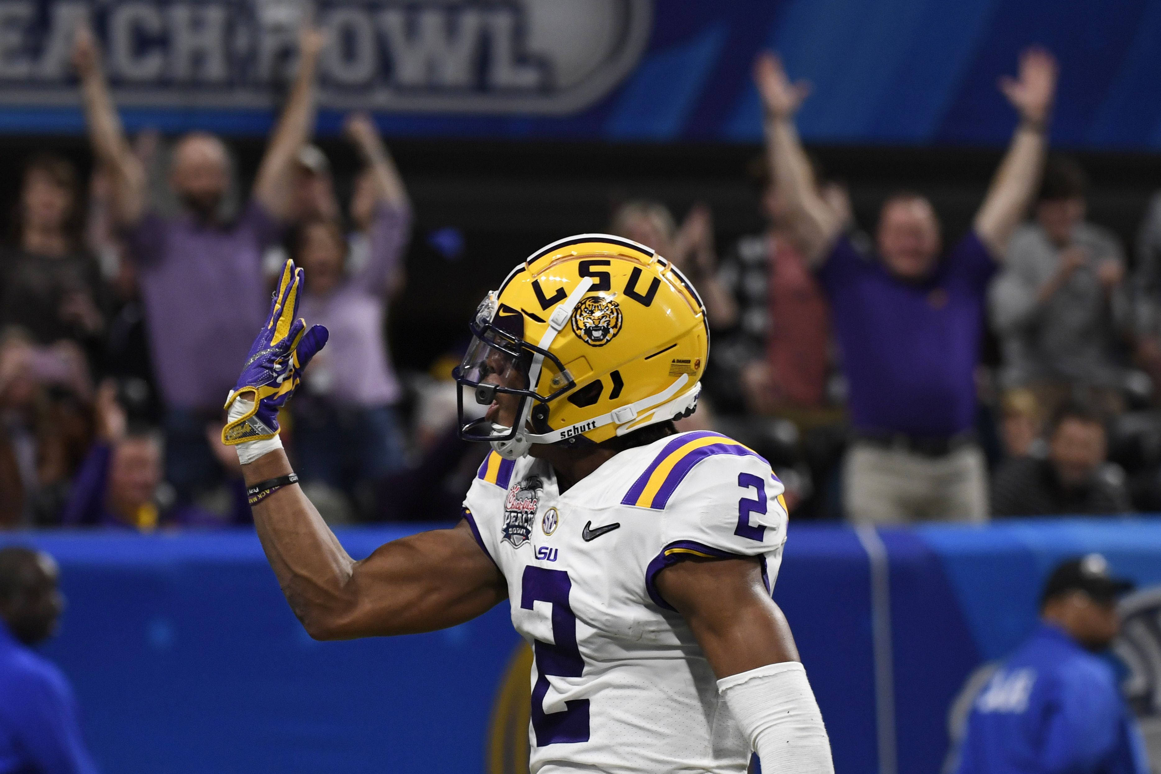 Justin Jefferson 碗賽傳球紀錄 壁紙 — LSU 美式足球員 2 號身穿白色和紫色球衣，在夜晚高舉手臂向歡呼的人群慶祝。