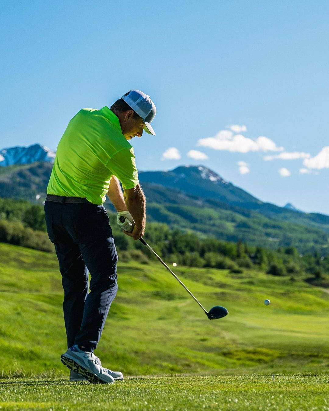 Justin Leonard 穩健揮杆 壁紙 — 一位穿著亮綠色襯衫的高爾夫球手在陽光明媚的球場上揮桿，背景是白雪皚皚的山脈。