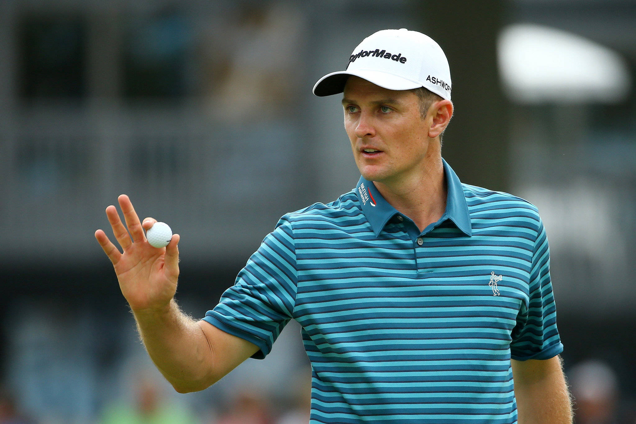 Justin Rose 手持高爾夫球 壁紙 — 一位專注的男性高爾夫球手穿著藍色條紋Polo衫，在模糊的球場上做出手勢時握著高爾夫球。