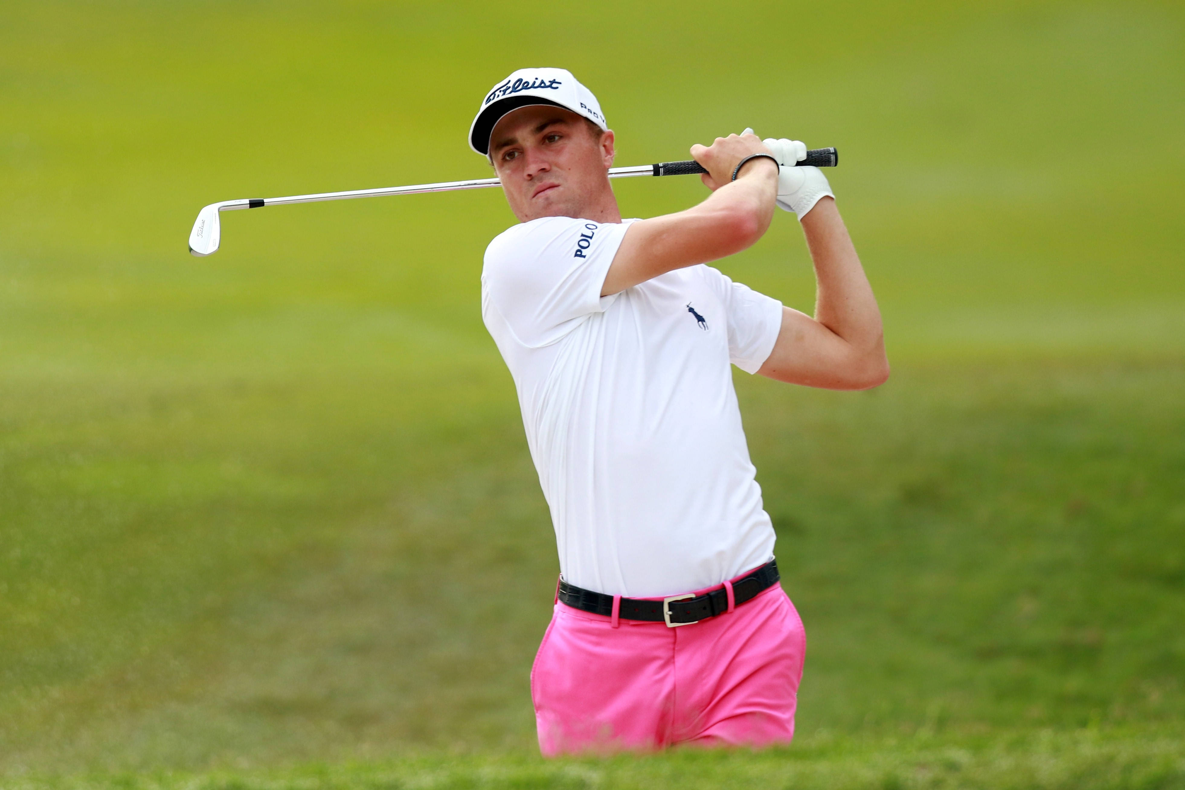 Justin Thomas 穿著粉紅褲子 壁紙 — 一位身穿白色襯衫和亮粉色短褲的男性高爾夫球手在鬱鬱蔥蔥的球場上揮桿。