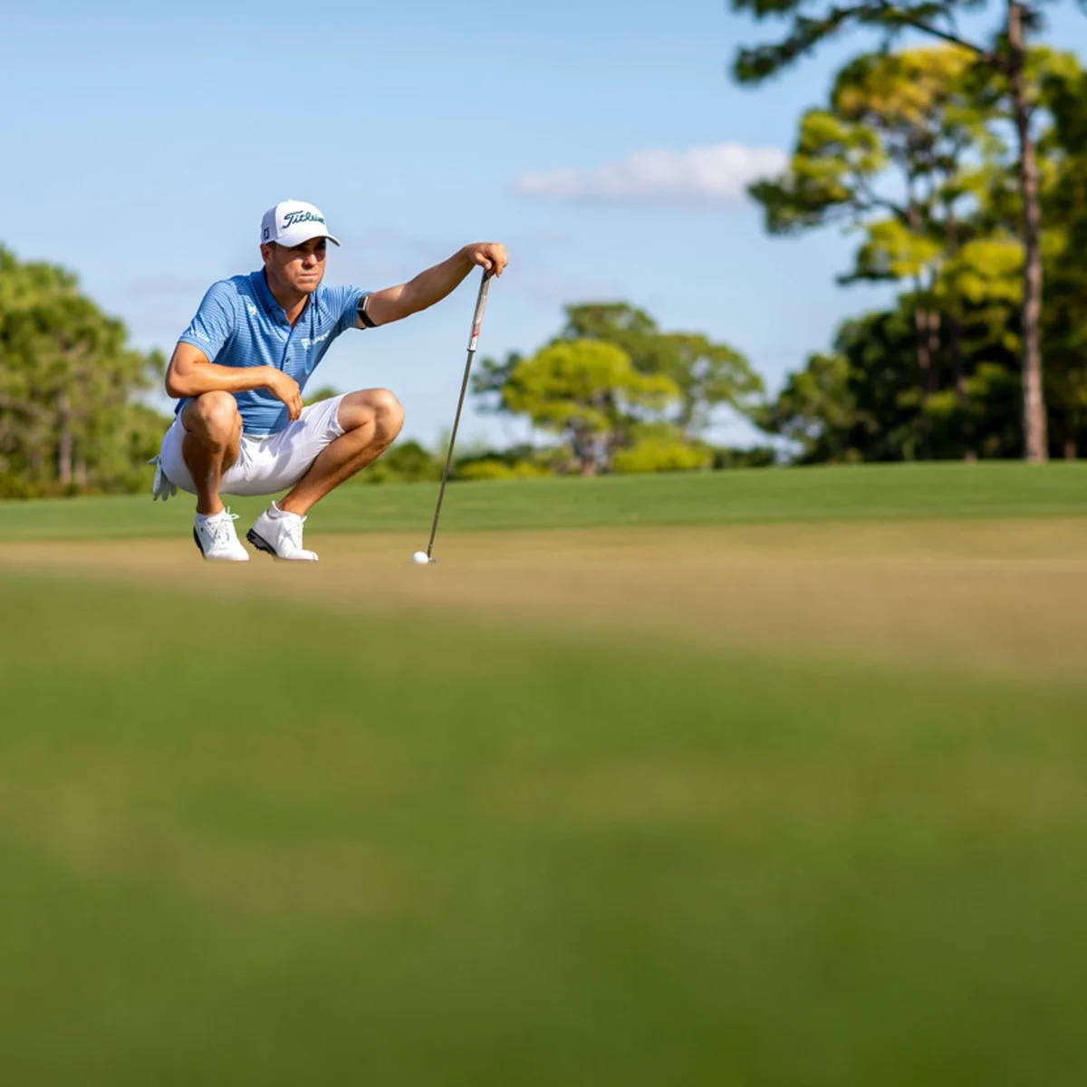 Justin Thomas 在高爾夫球場上 壁紙 — 一名高爾夫球手在陽光明媚的果嶺上蹲下，在晴朗的藍天下專注地瞄準推桿。