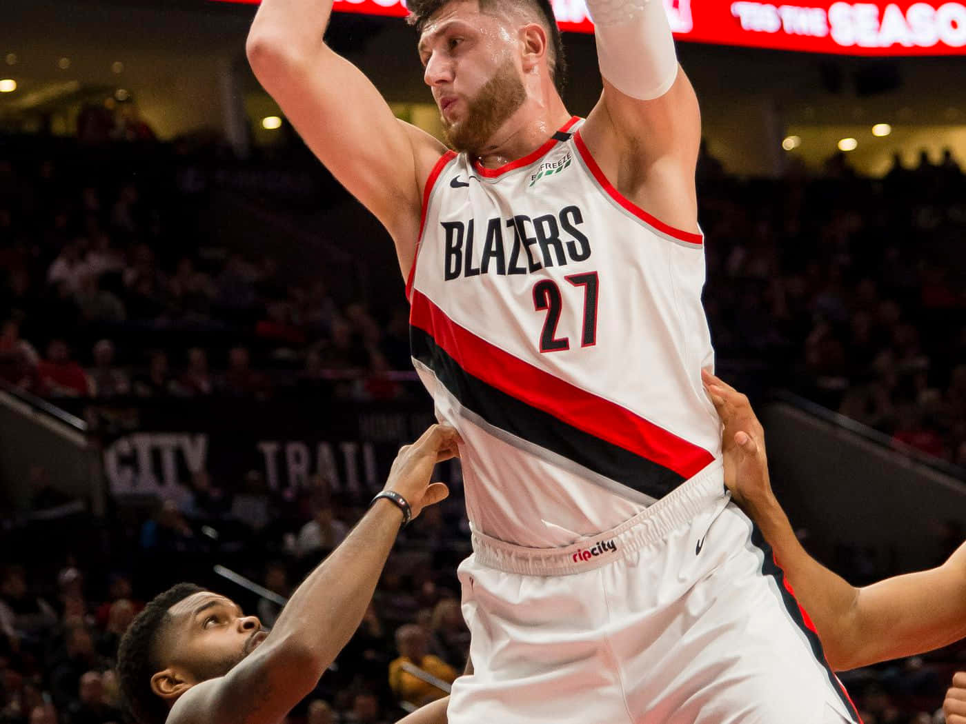 Jusuf Nurkic 場上英姿 壁紙 — 一名身穿白色 Blazers 球衣的籃球運動員高高躍起投籃，防守球員在擠滿觀眾的場館中伸手阻擋。