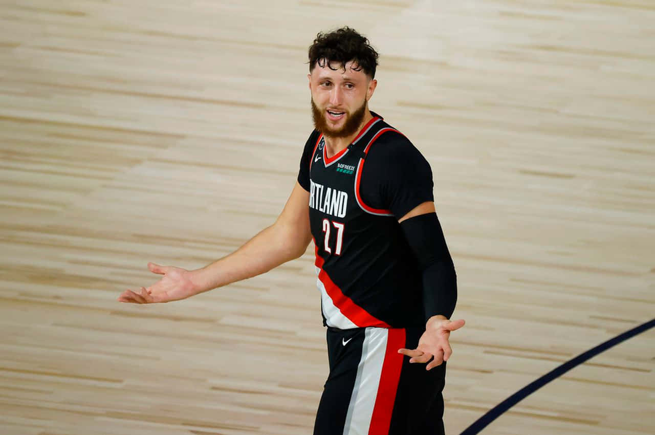 Jusuf Nurkic 對戰印第安納溜馬隊 壁紙 — 一名身穿波特蘭拓荒者球衣的籃球運動員在木地板上張開雙手做手勢。